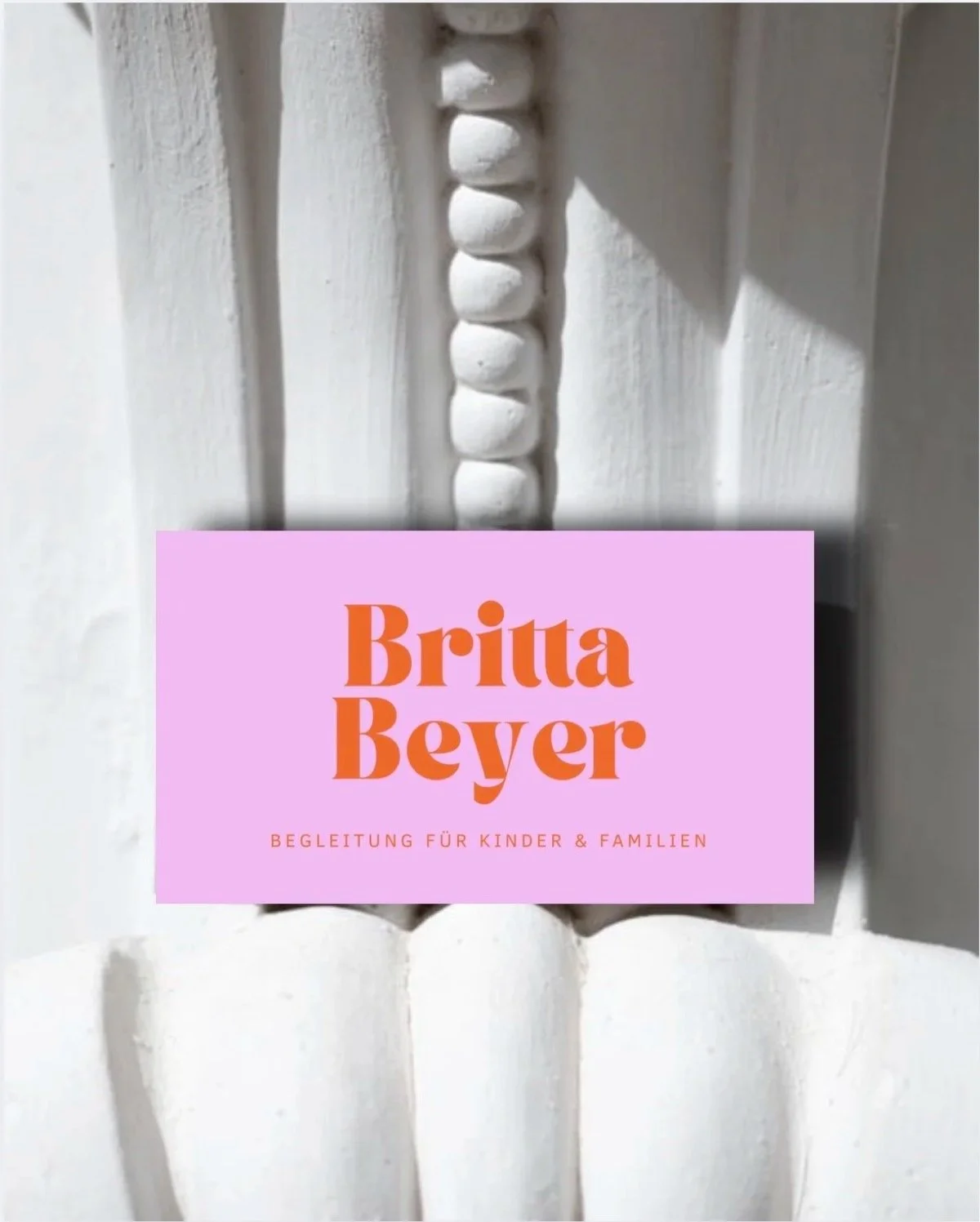 Weiße Holzverzierung mit geschnitzten Mustern und einem pinken Textfeld mit dem Namen Britta Beyer und dem Untertitel Begleitung für Kinder & Familien.