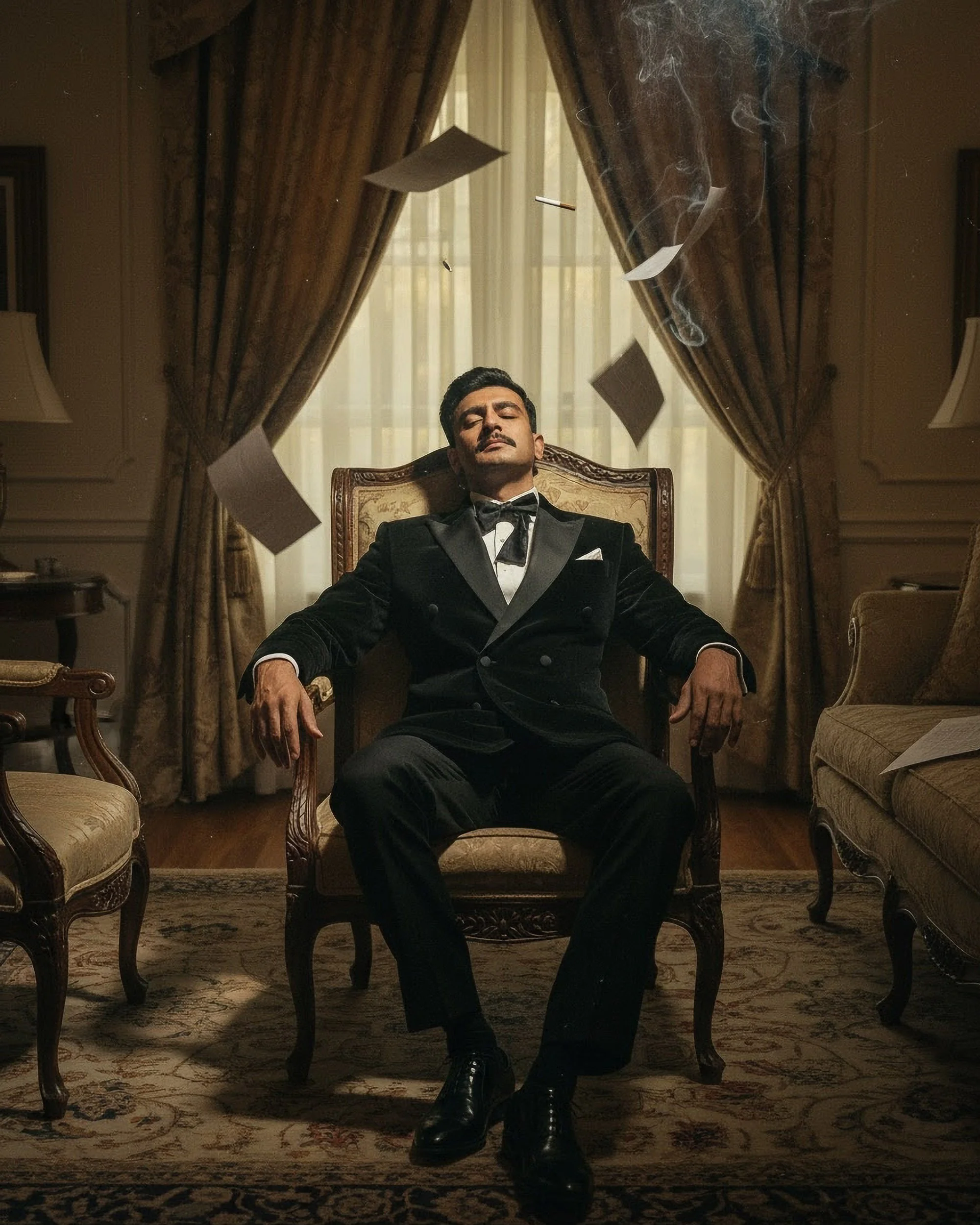 A man in a tuxedo with a bow tie is sitting in an ornate wooden chair in a room with curtains and furniture. Papers are flying around him, and he is sitting with his eyes closed and a serious expression.