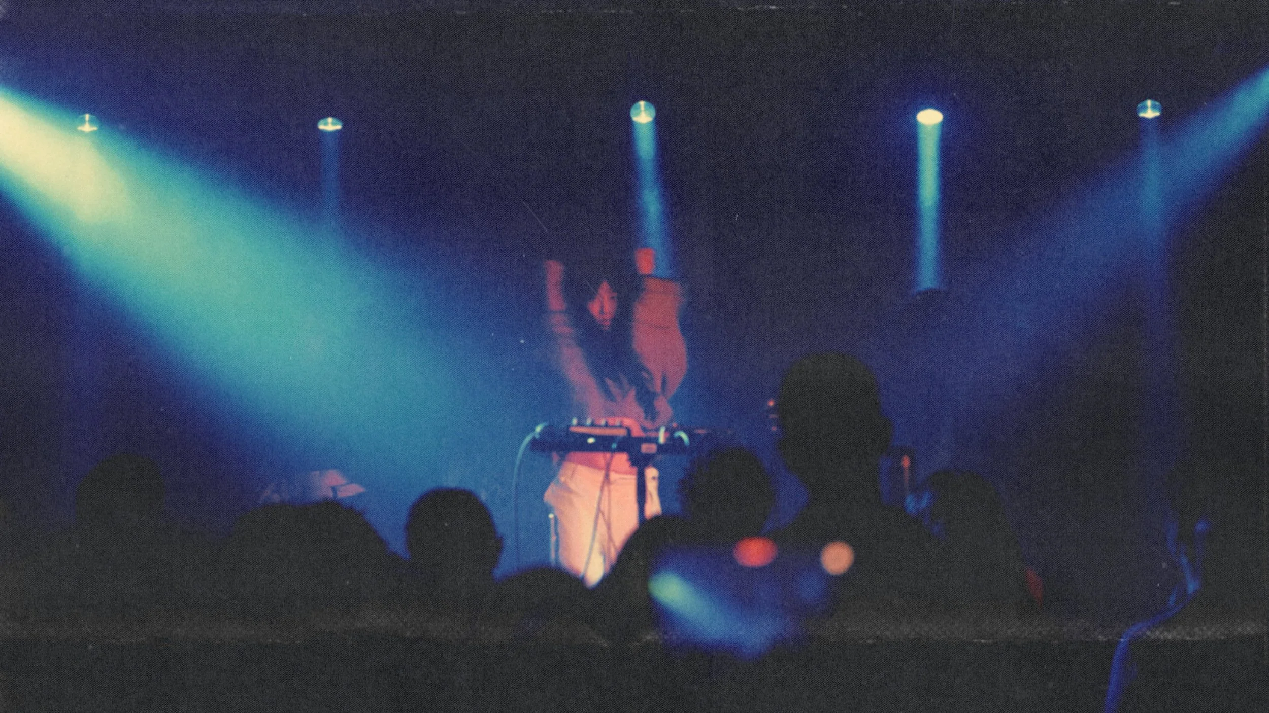 A DJ performing on stage with blue and purple lighting, surrounded by an audience.