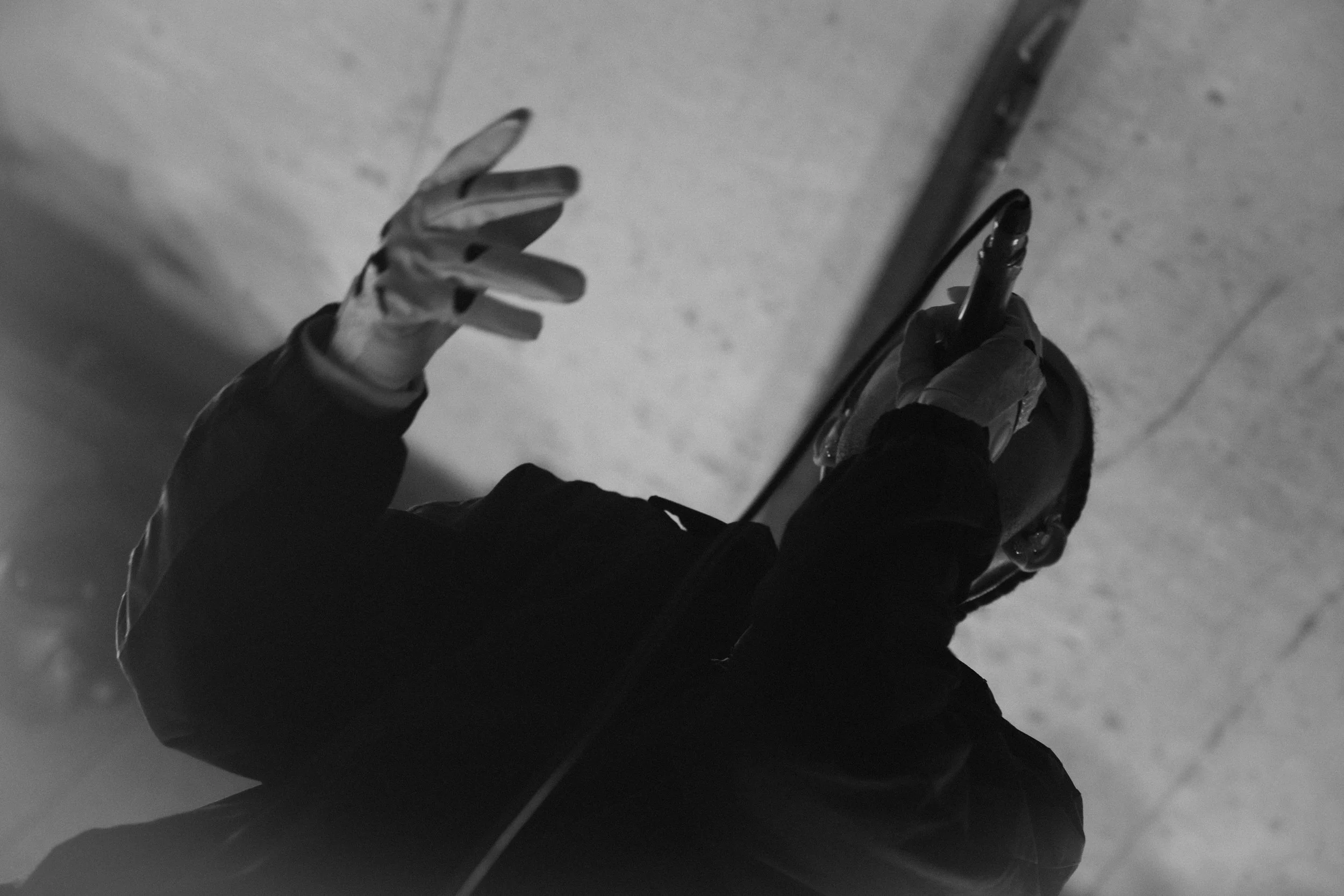 A person wearing a dark jacket is holding a skateboard with one hand, standing on a concrete surface, with their other hand holding a smartphone