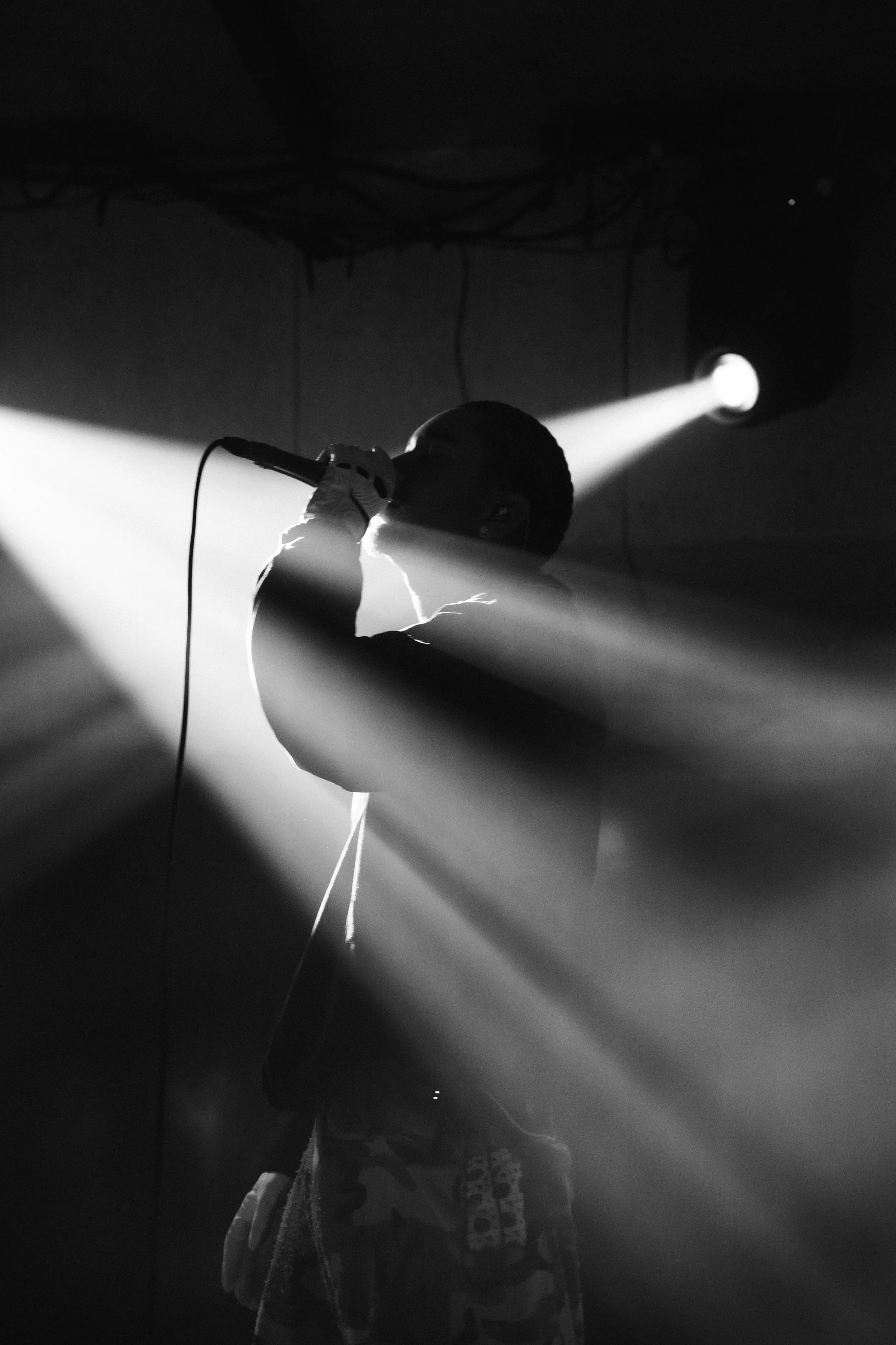 A person holding a microphone on stage with a spotlight shining on them, in black and white.