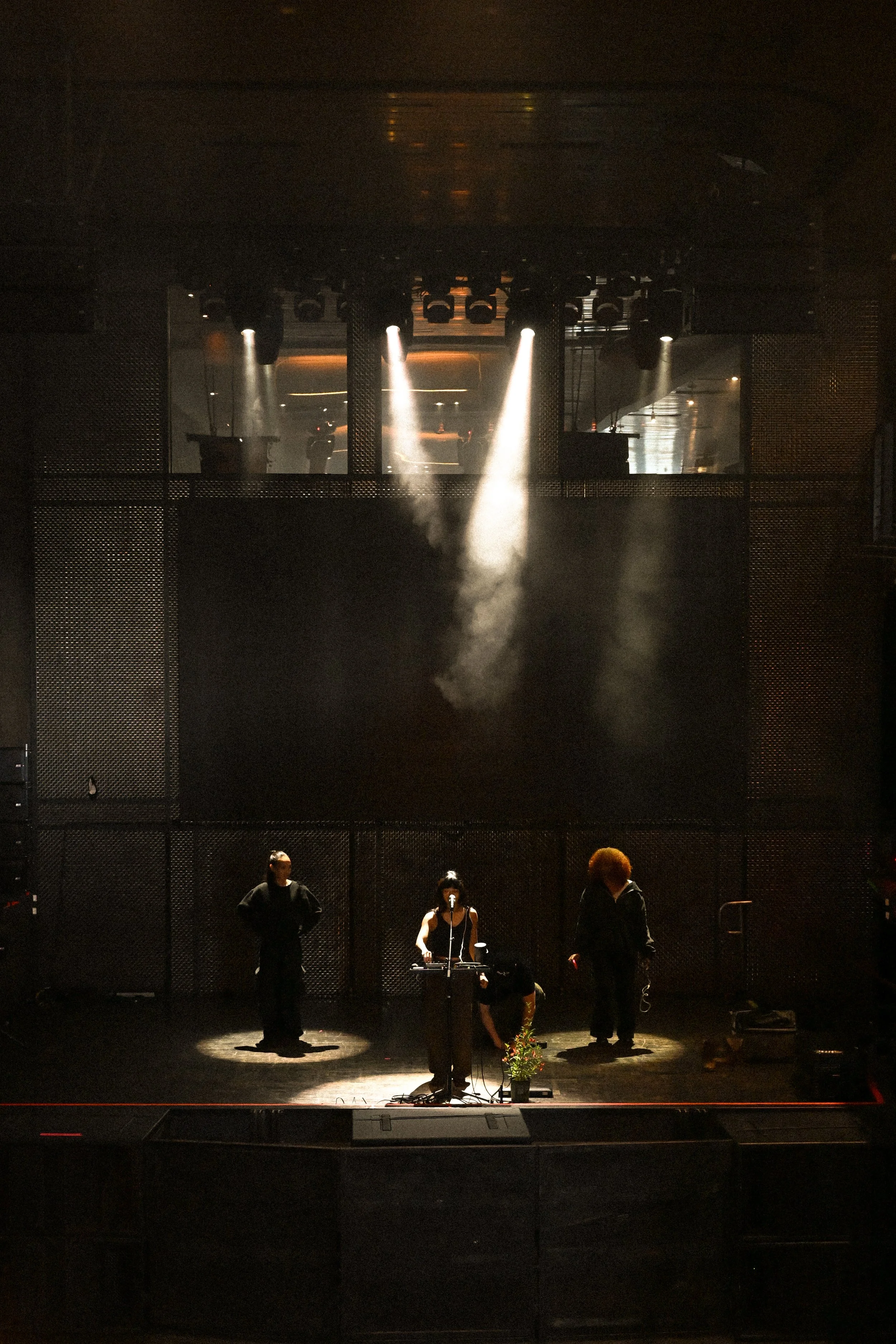 A concert stage with stage lights and sound equipment visible in the background, and miniature figures of people preparing for a performance in the foreground.