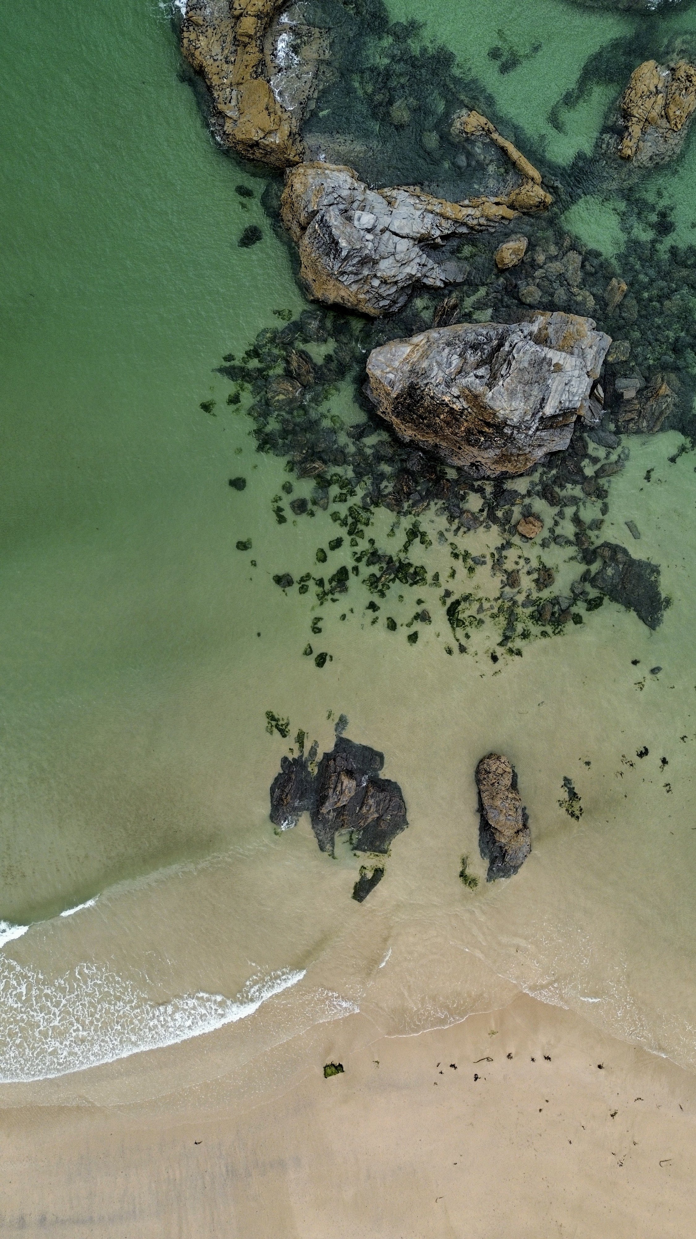 Aerial view of a beach with rocks, green water, and sandy shore.