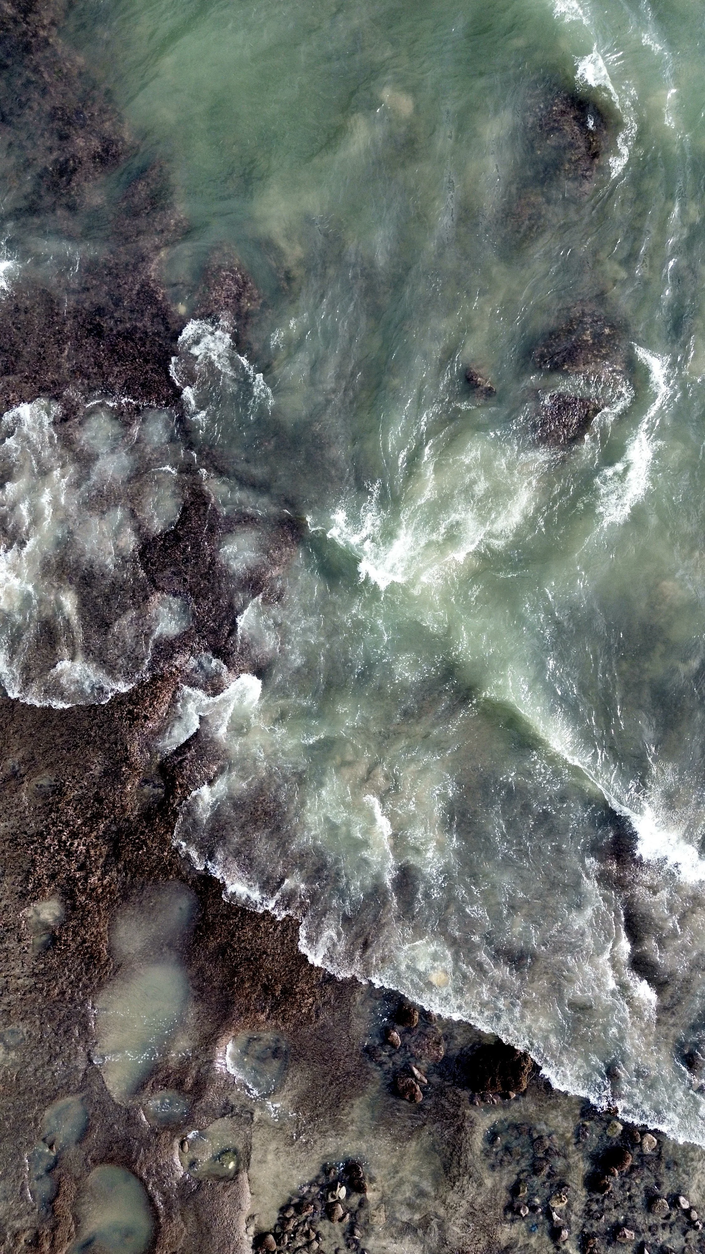 A view of a rocky shoreline with small waves washing over stones and rocks in the water.