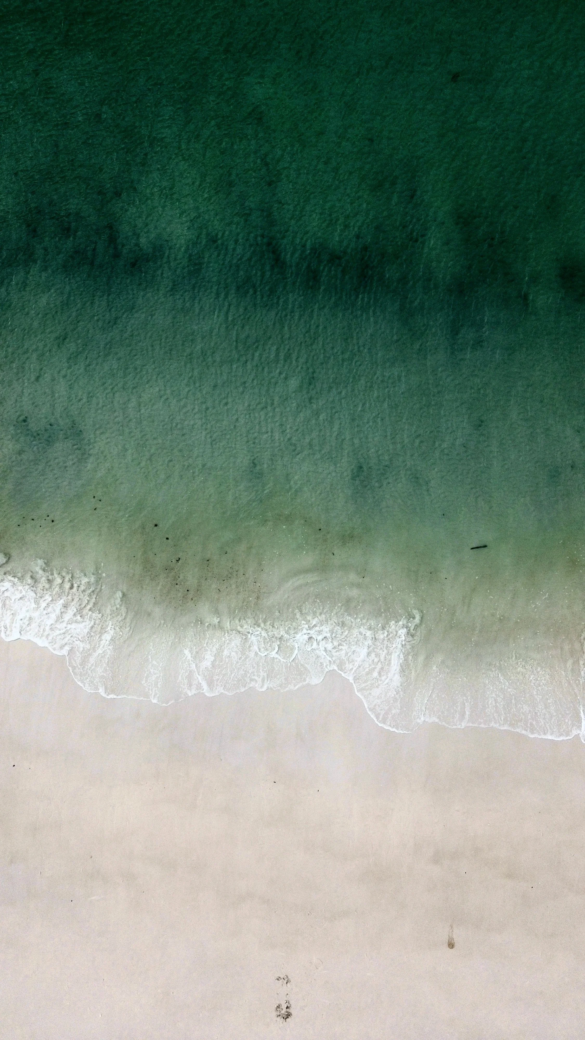 Aerial view of a sandy beach with waves washing onto the shore, overlooking the ocean with greenish water.