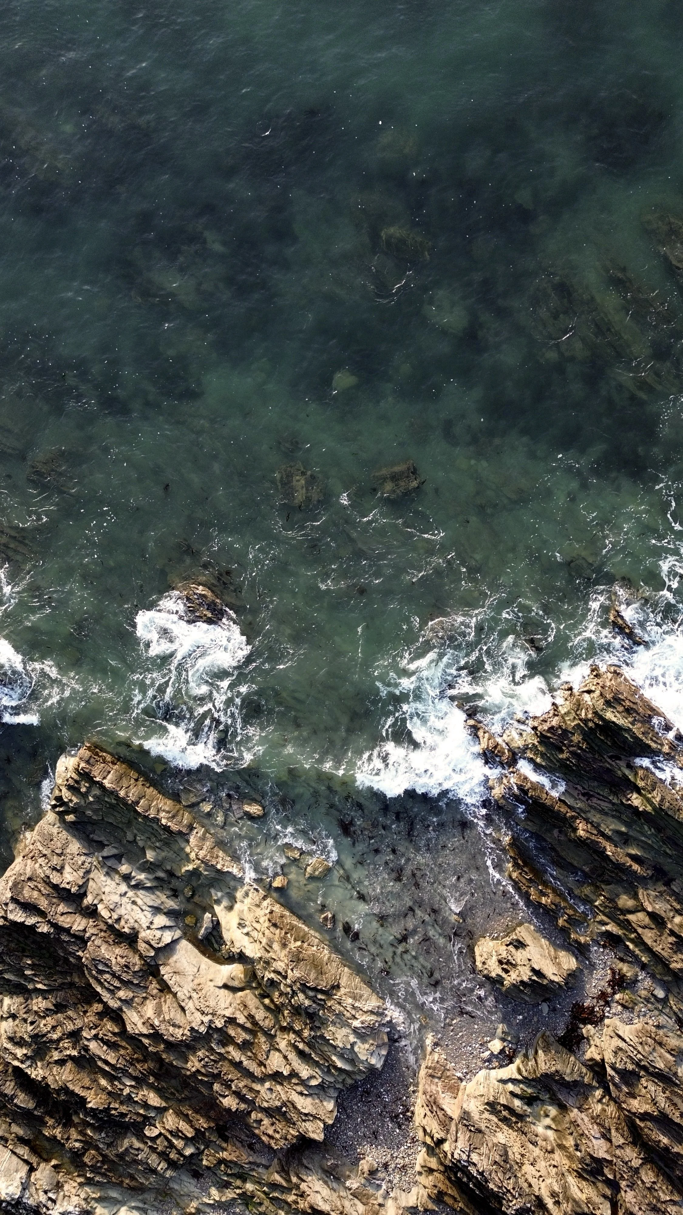 Aerial view of the ocean with rocks and waves crashing against them.