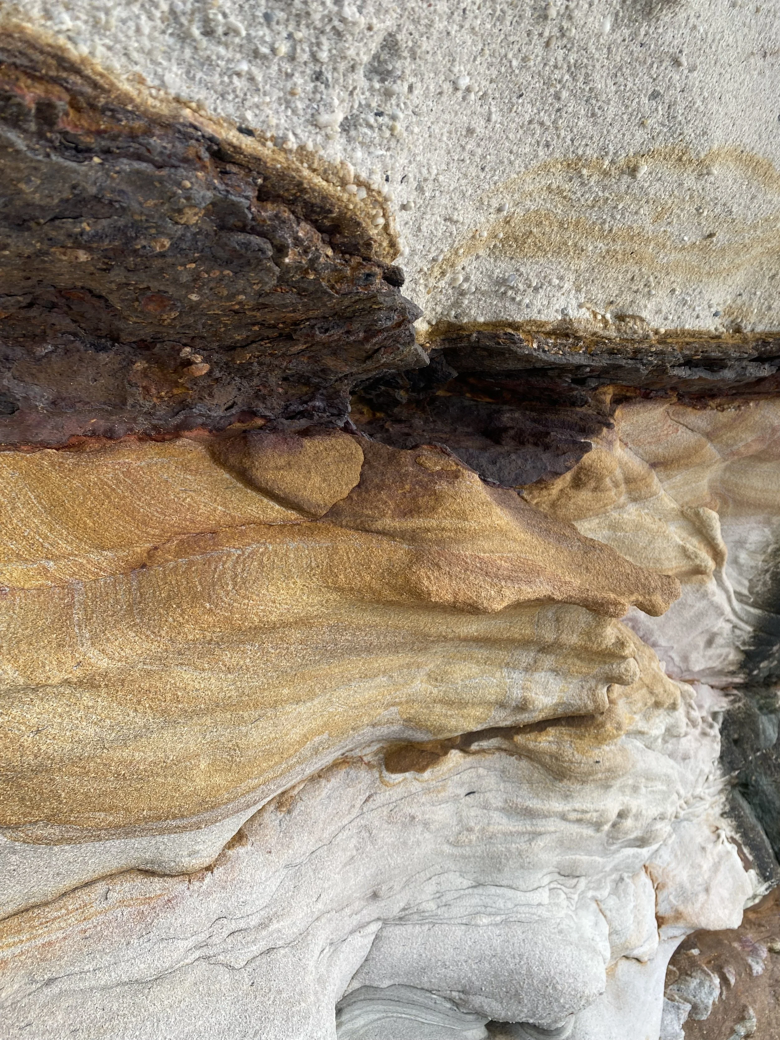 Close-up of layered rocks and sediment in shades of beige, brown, and gray, showing natural striations and textures.