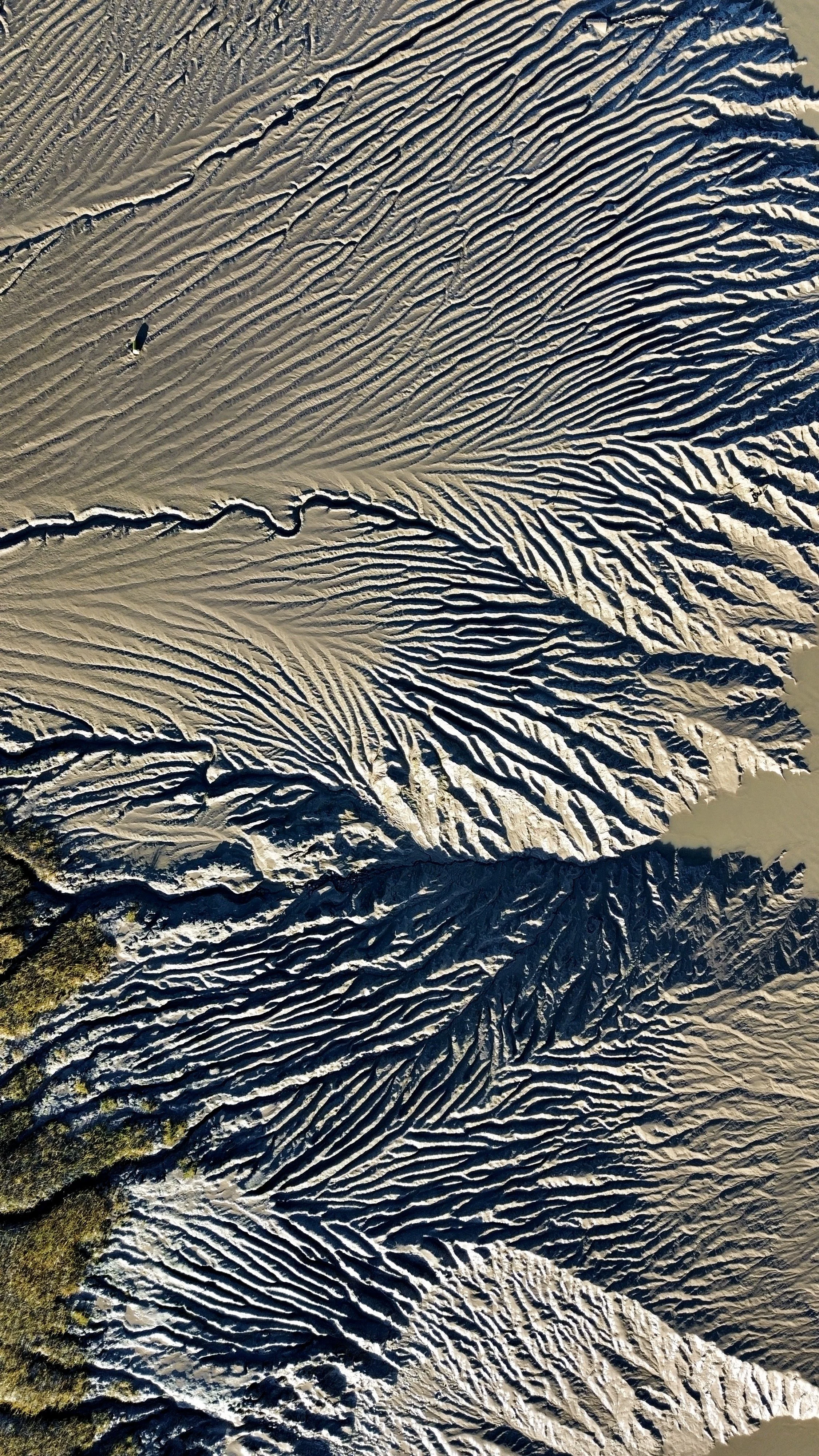 Aerial view of a white sandy desert with numerous intricate, winding patterns and ridges in the sand, with some areas casting shadows.
