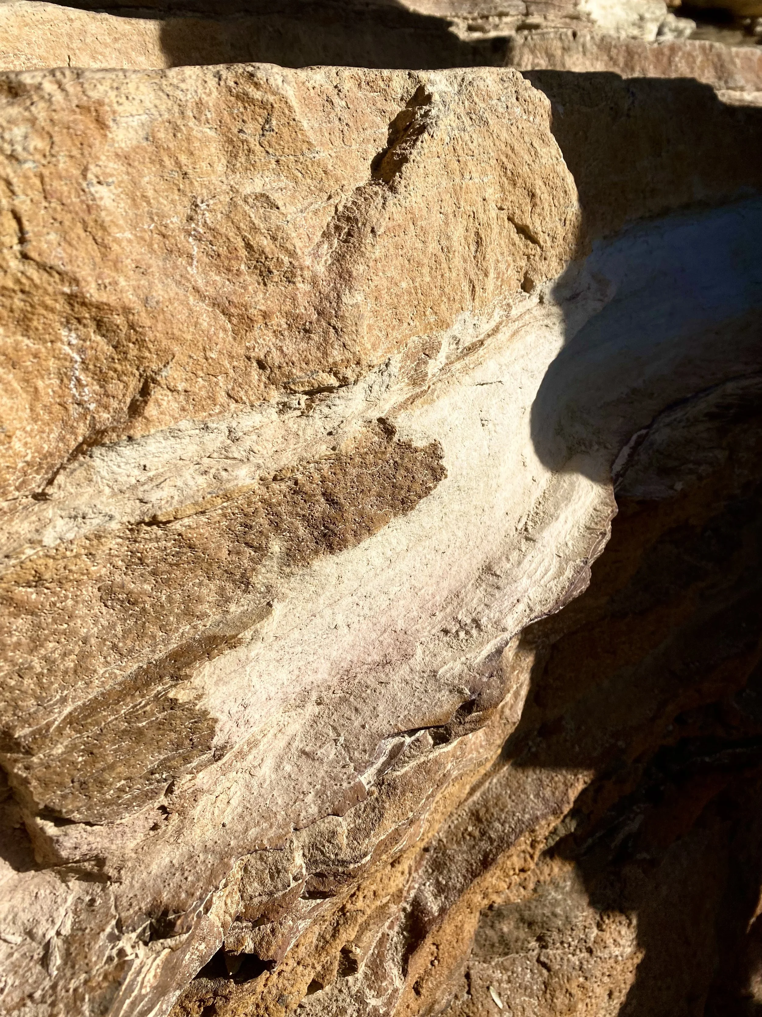 Close-up of a stack of rough, textured desert rocks with warm, earthy tones and shadows cast by sunlight.