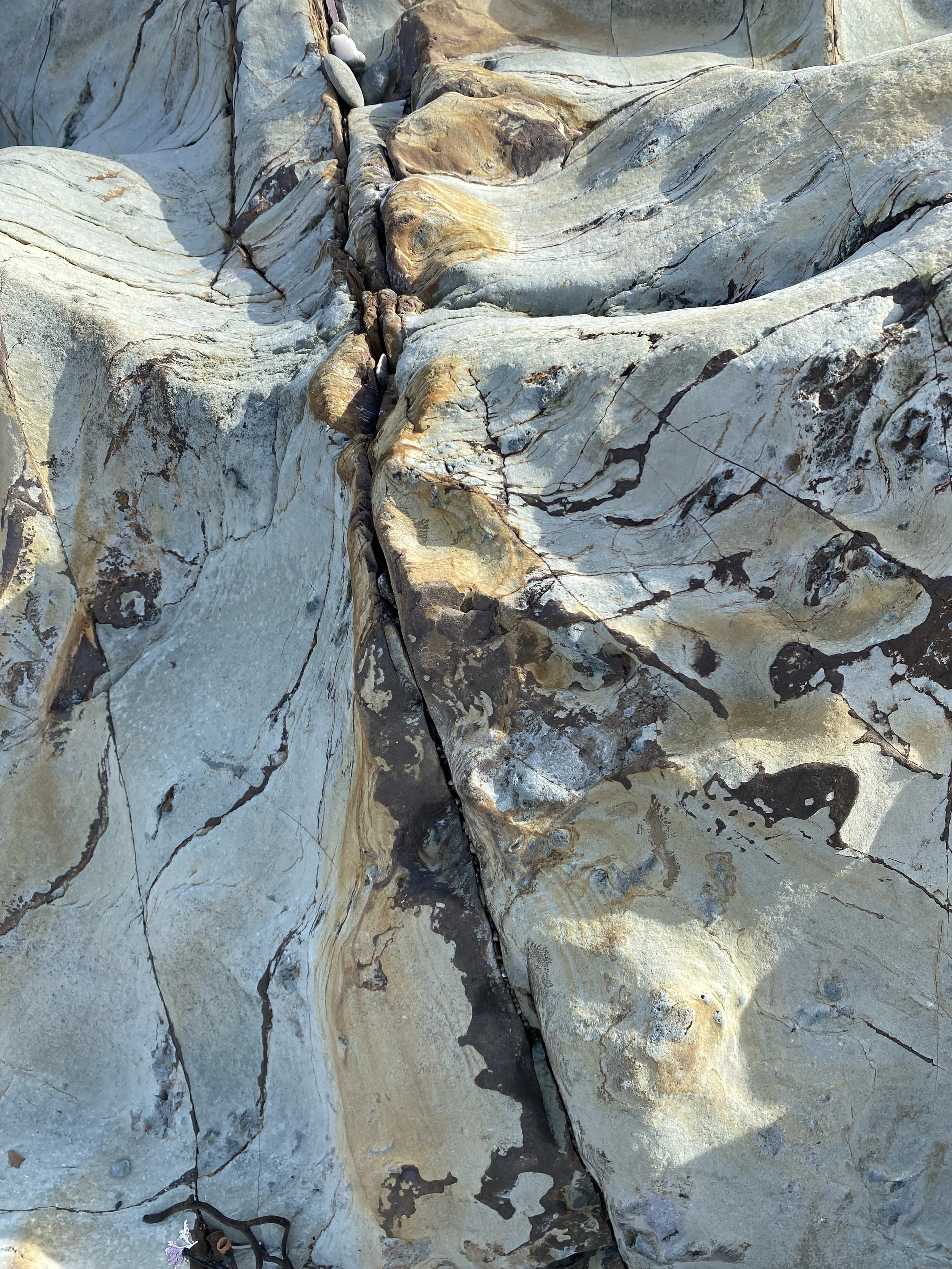 Close-up view of layered, weathered rocks with varying shades of gray, brown, and black, featuring cracks and patterns in a natural landscape.