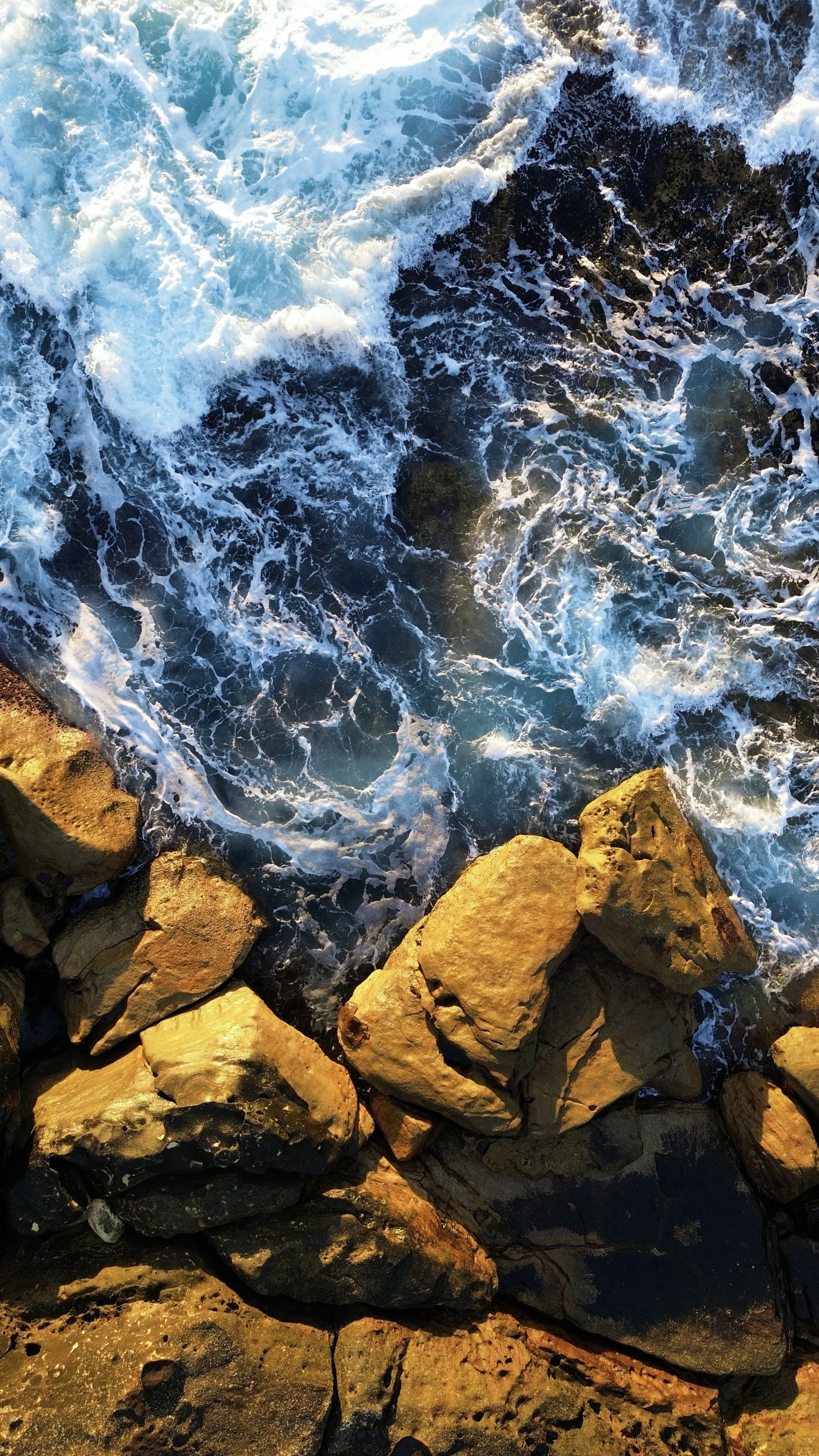 Waves crashing against rocks along a shoreline, with foam and water splashing over the rocks.