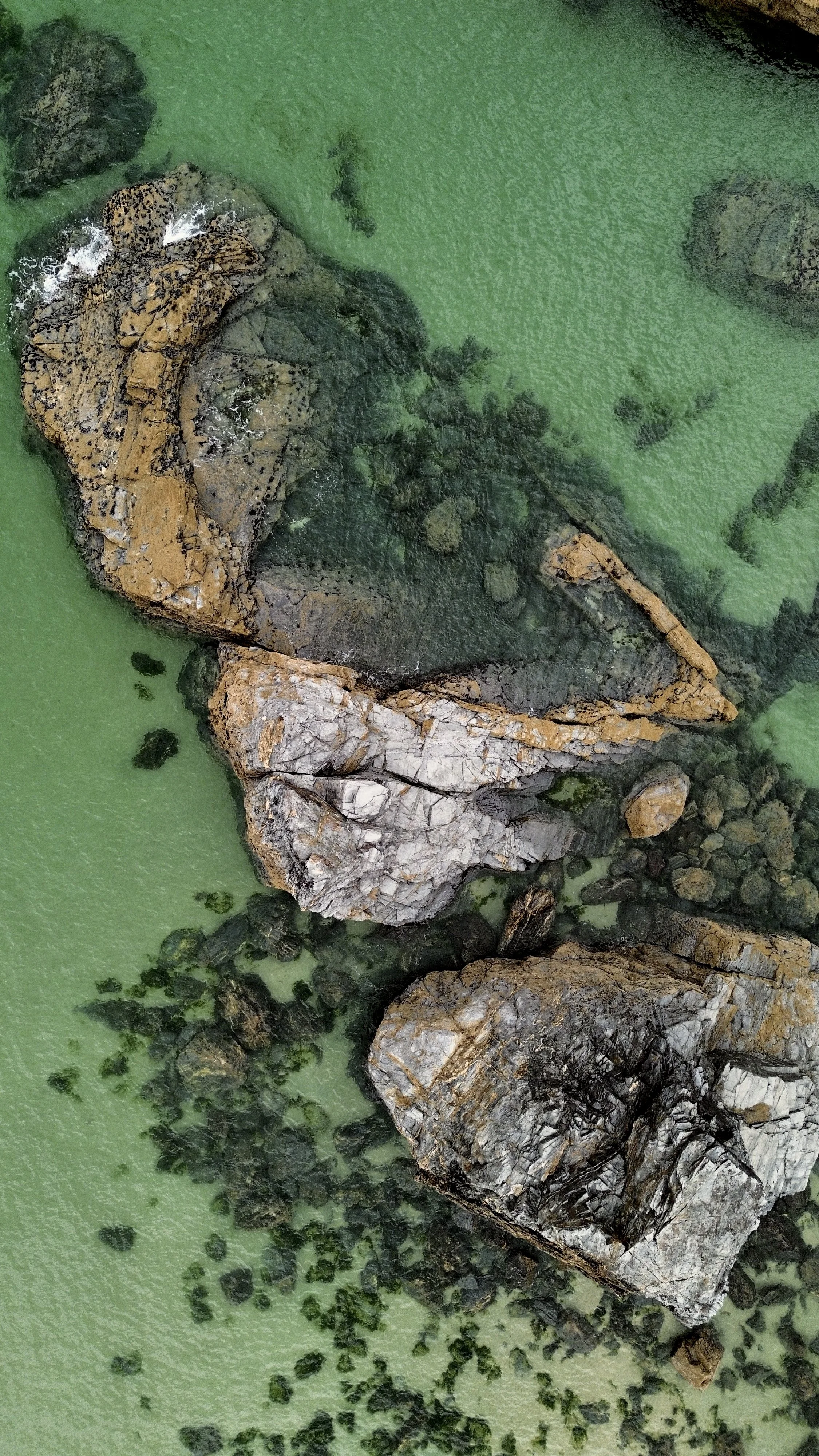 Aerial view of large rocks in turquoise water with smaller rocks scattered around.
