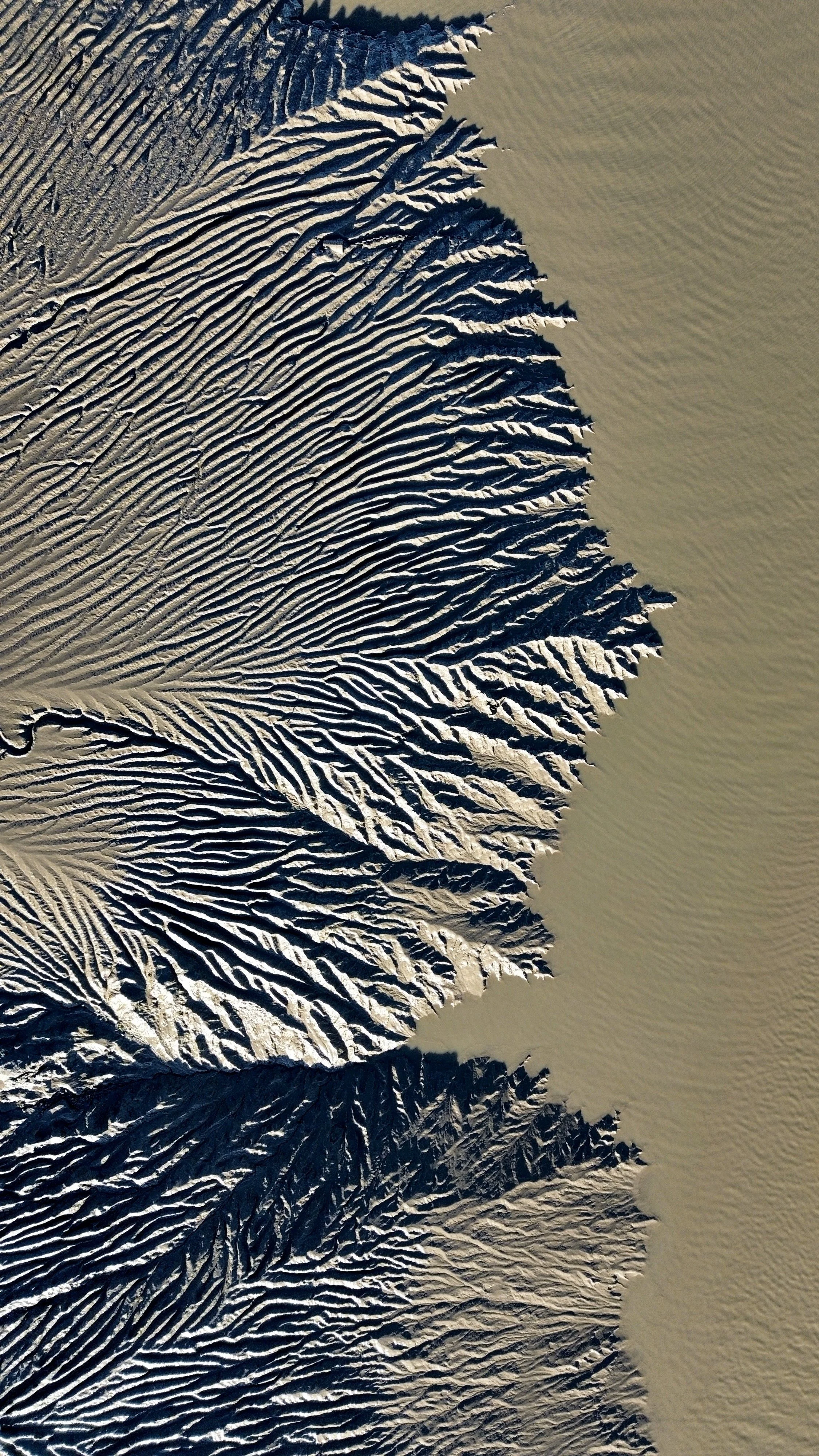 Aerial view of sand dunes with snow or ice, showing intricate ridges and patterns on a desert landscape.