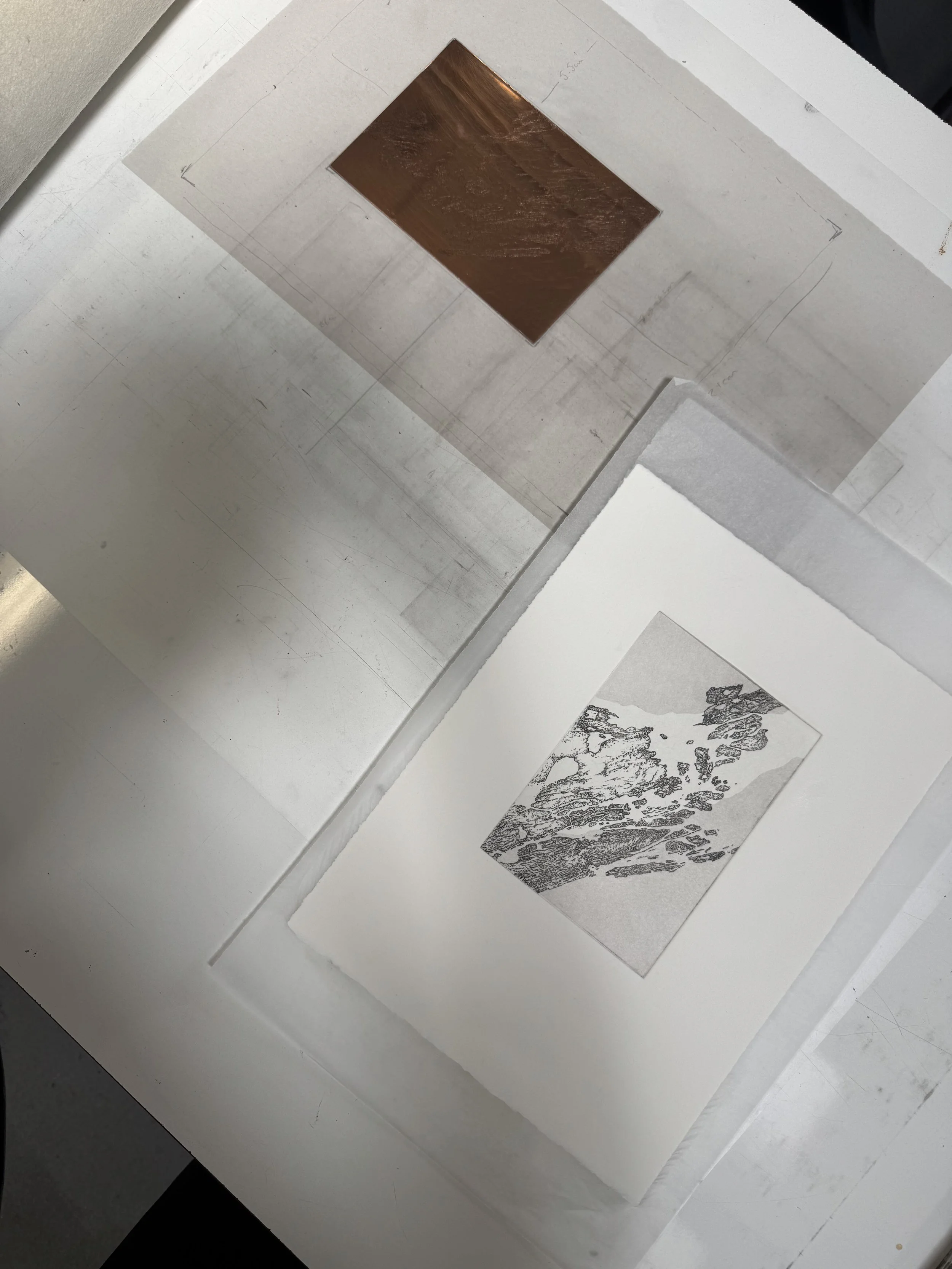 A wooden square panel mounted on a flat surface with hand-drawn markings around it, next to some printed black and white mountain landscape photos.