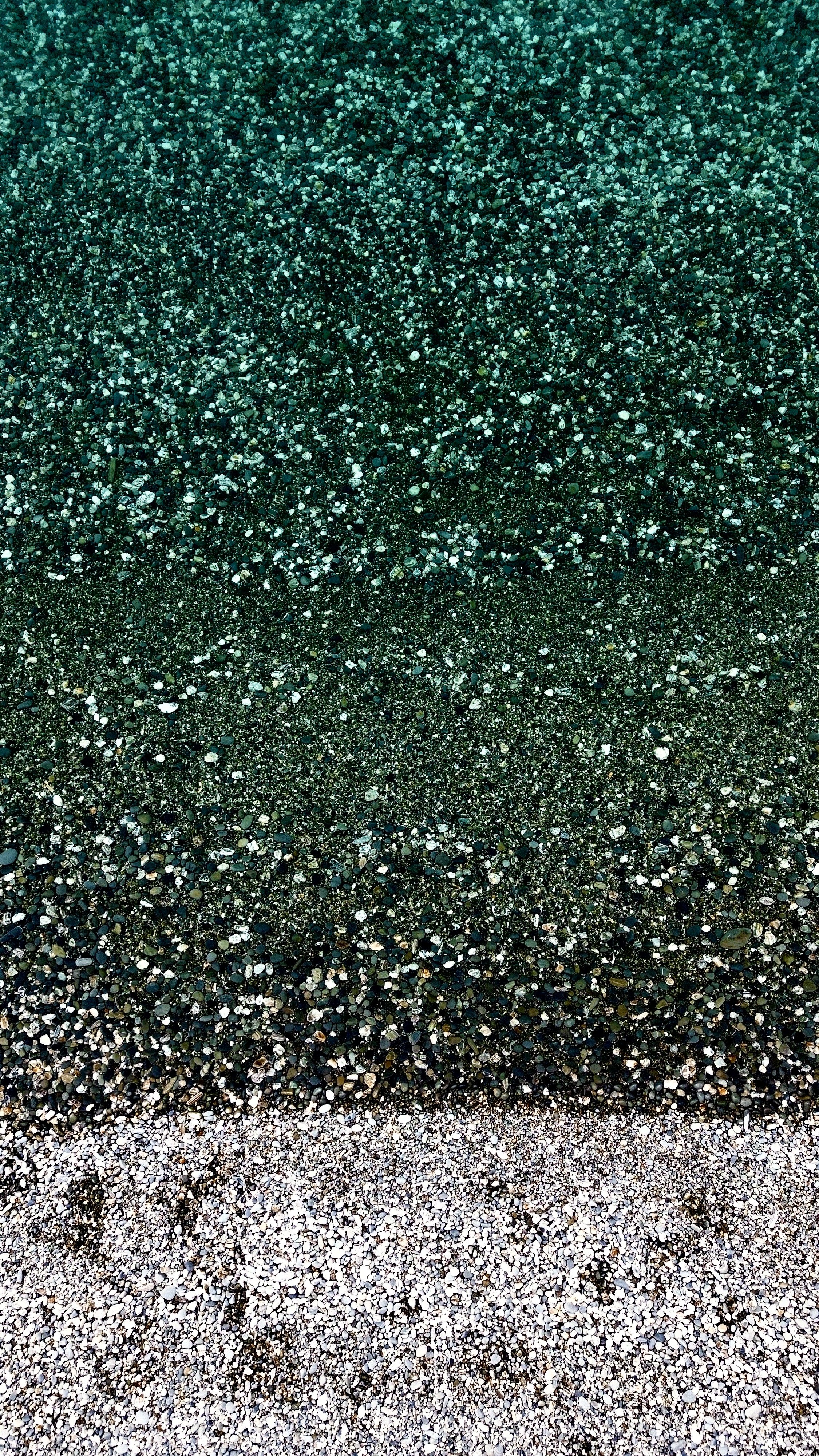 A close-up view of a multicolored gravel beach with layers of green, black, gray, and white gravel.