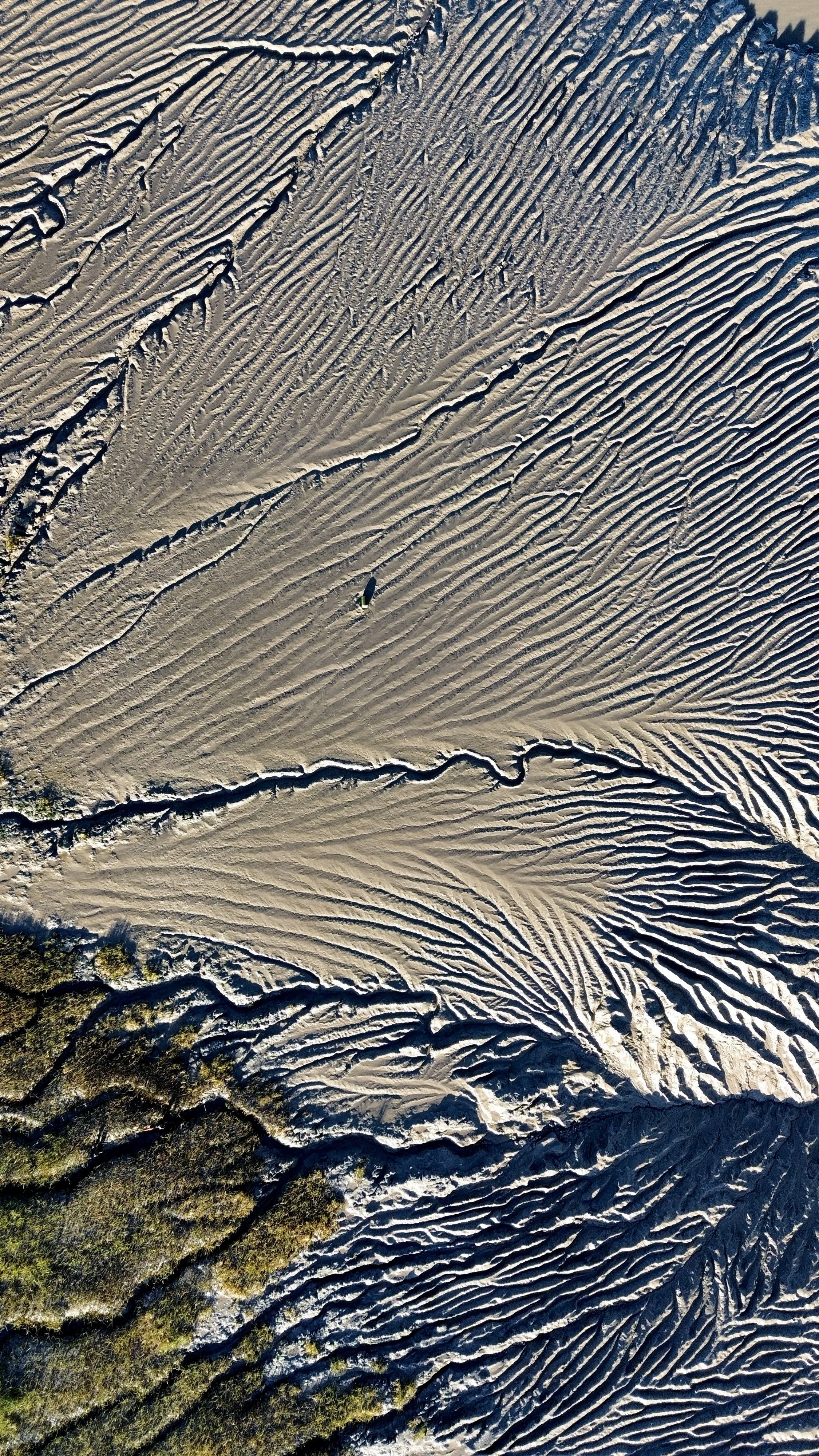 Aerial view of a sandy desert with intricate, wavy patterns and small patches of greenery along the edges.