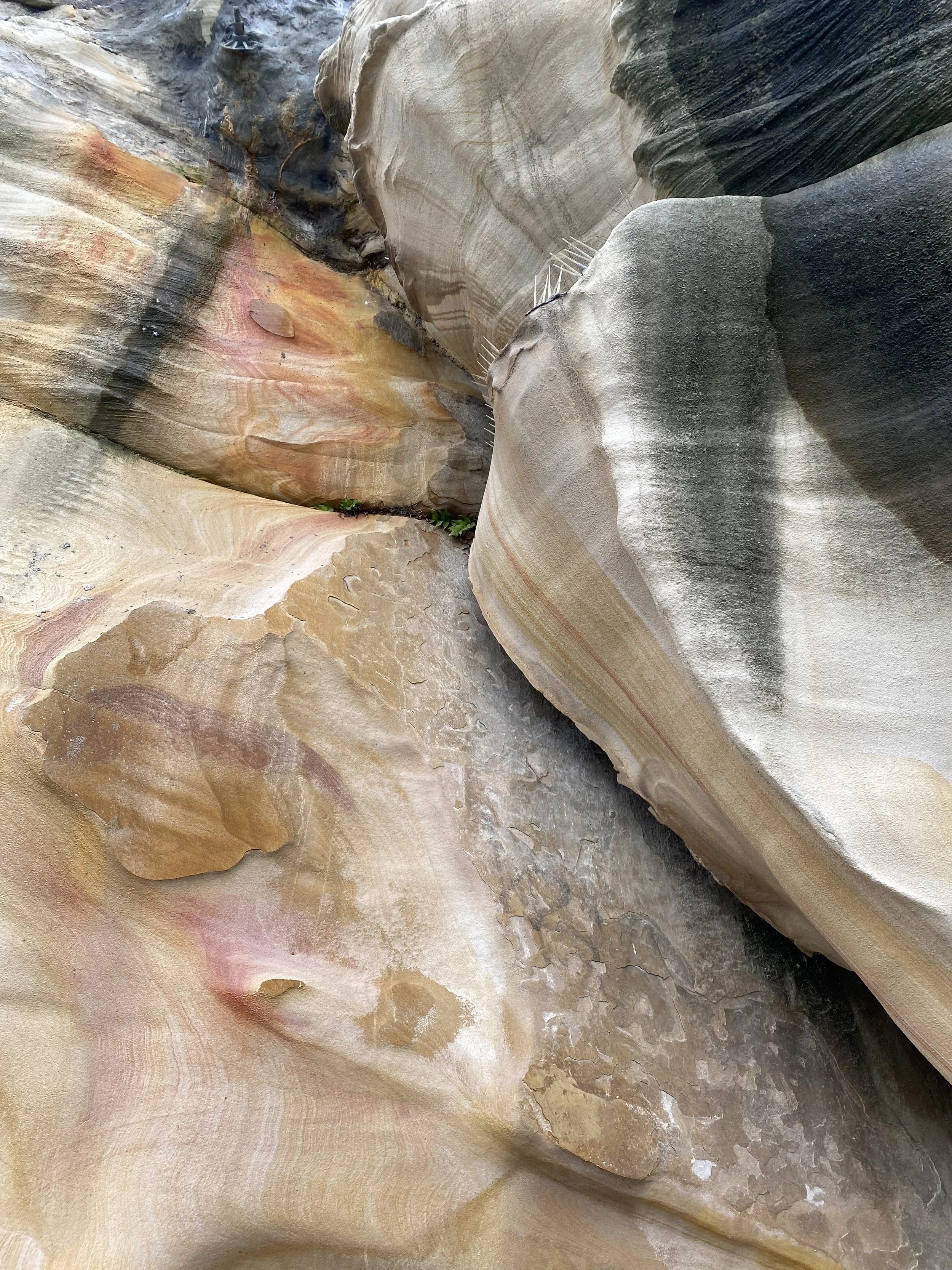 Close-up of layered, colorful, and textured rock formations with shades of beige, pink, brown, and black.