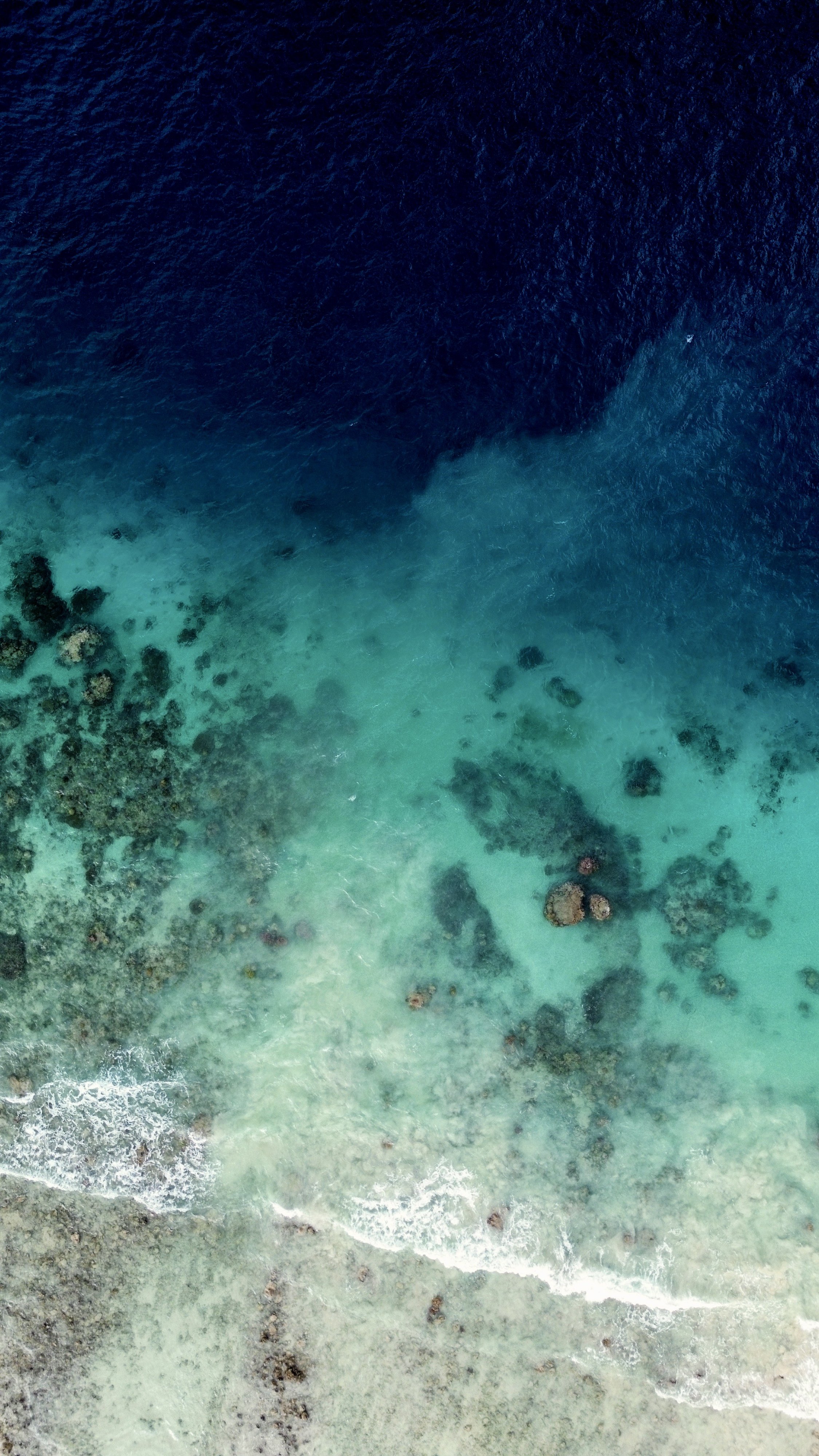 Aerial view of a beach with turquoise water, coral reefs, and rocks along the shoreline.