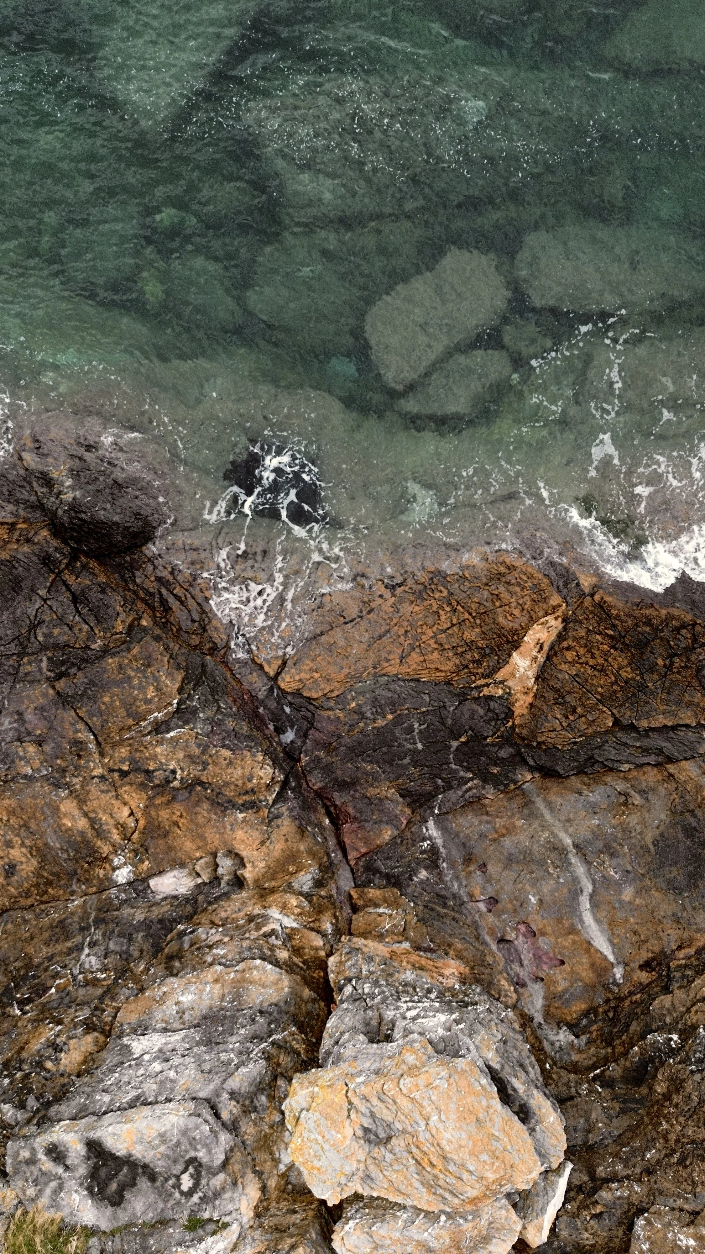 A view of rocks and stones along a shoreline, with clear water and some small waves.