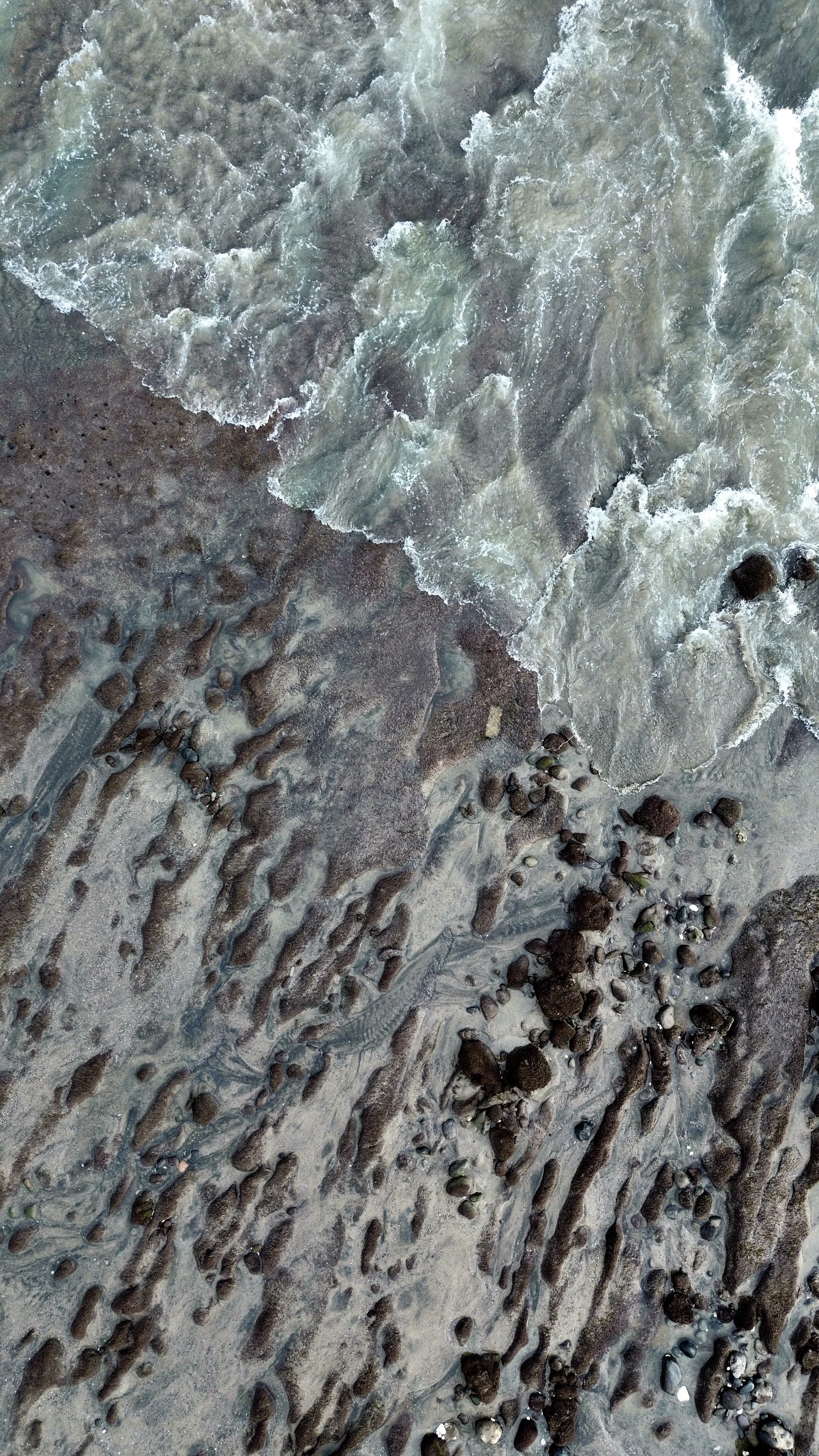 Close-up of sandy beach with rocks and shallow water waves.