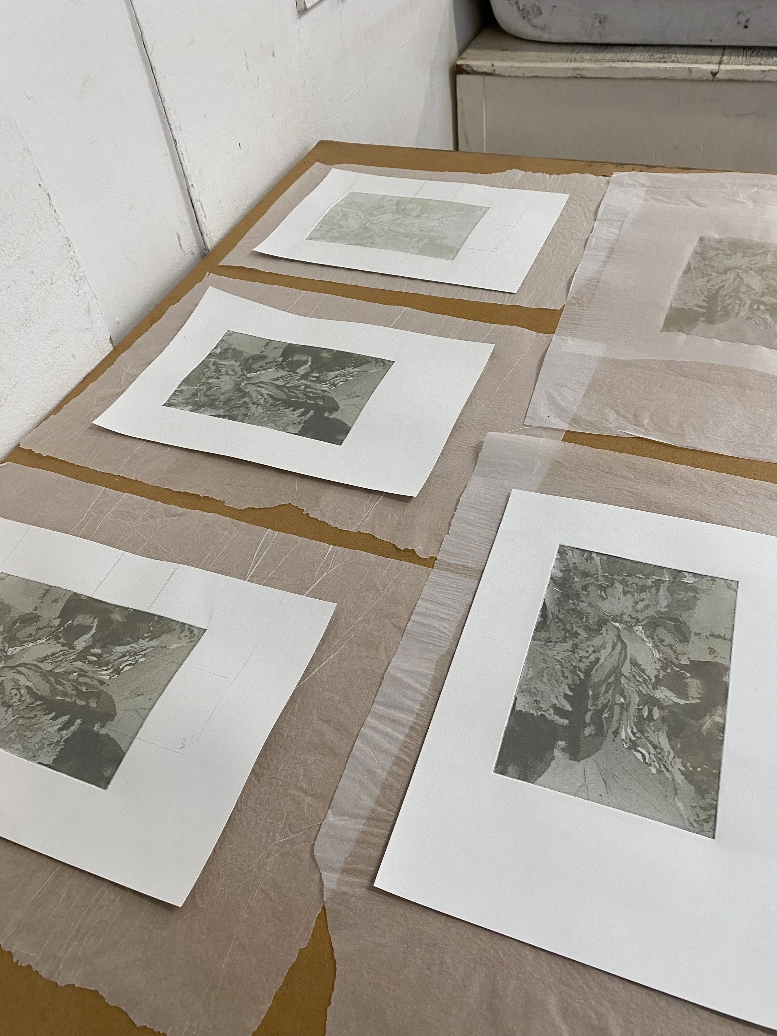 Photograph of printed sheets with marble pattern, laid on a surface covered with brown paper and tissue paper, near a white wall, possibly in a studio or workspace.