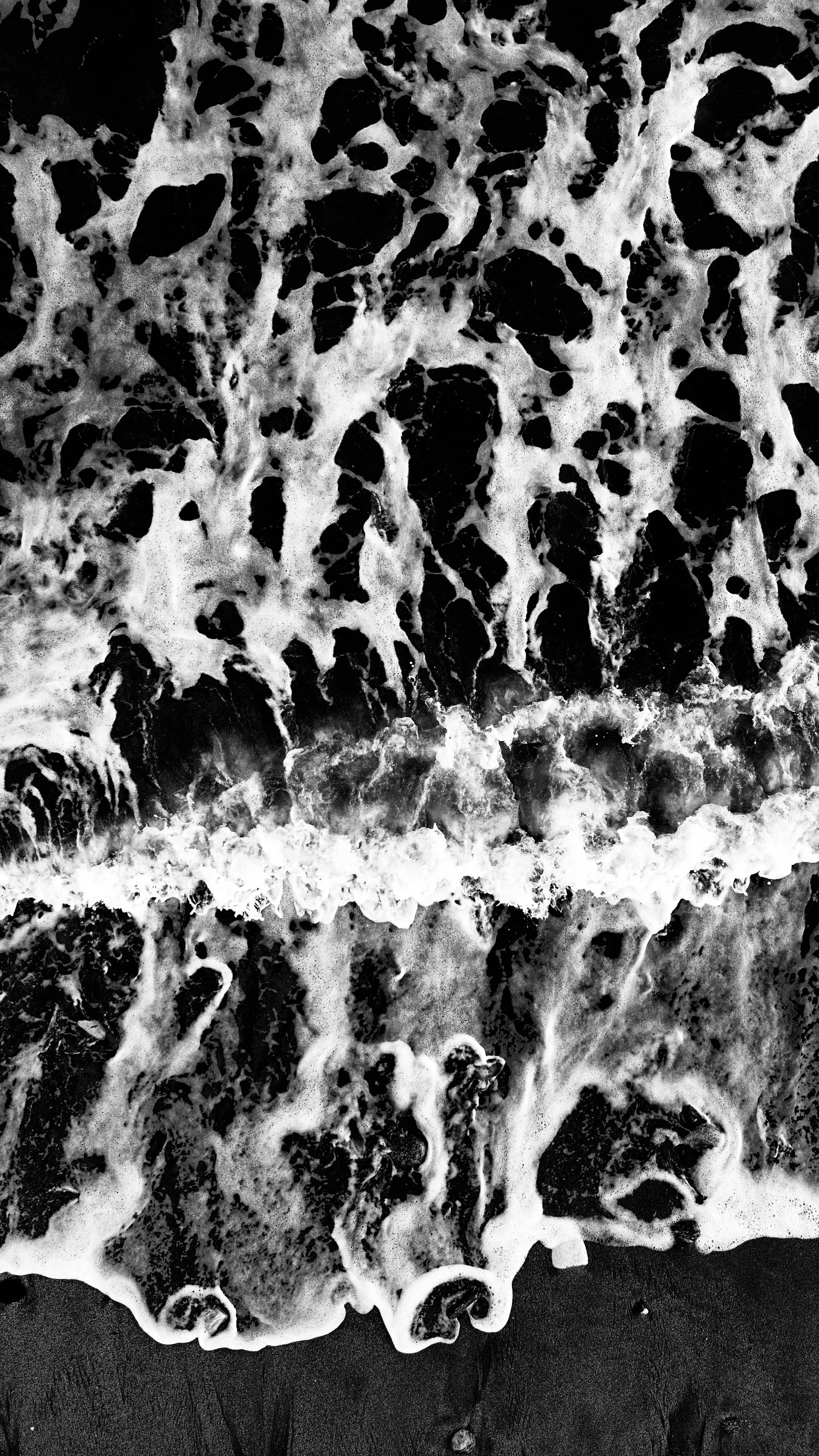 Black and white photo of foamy ocean waves crashing onto the shore.