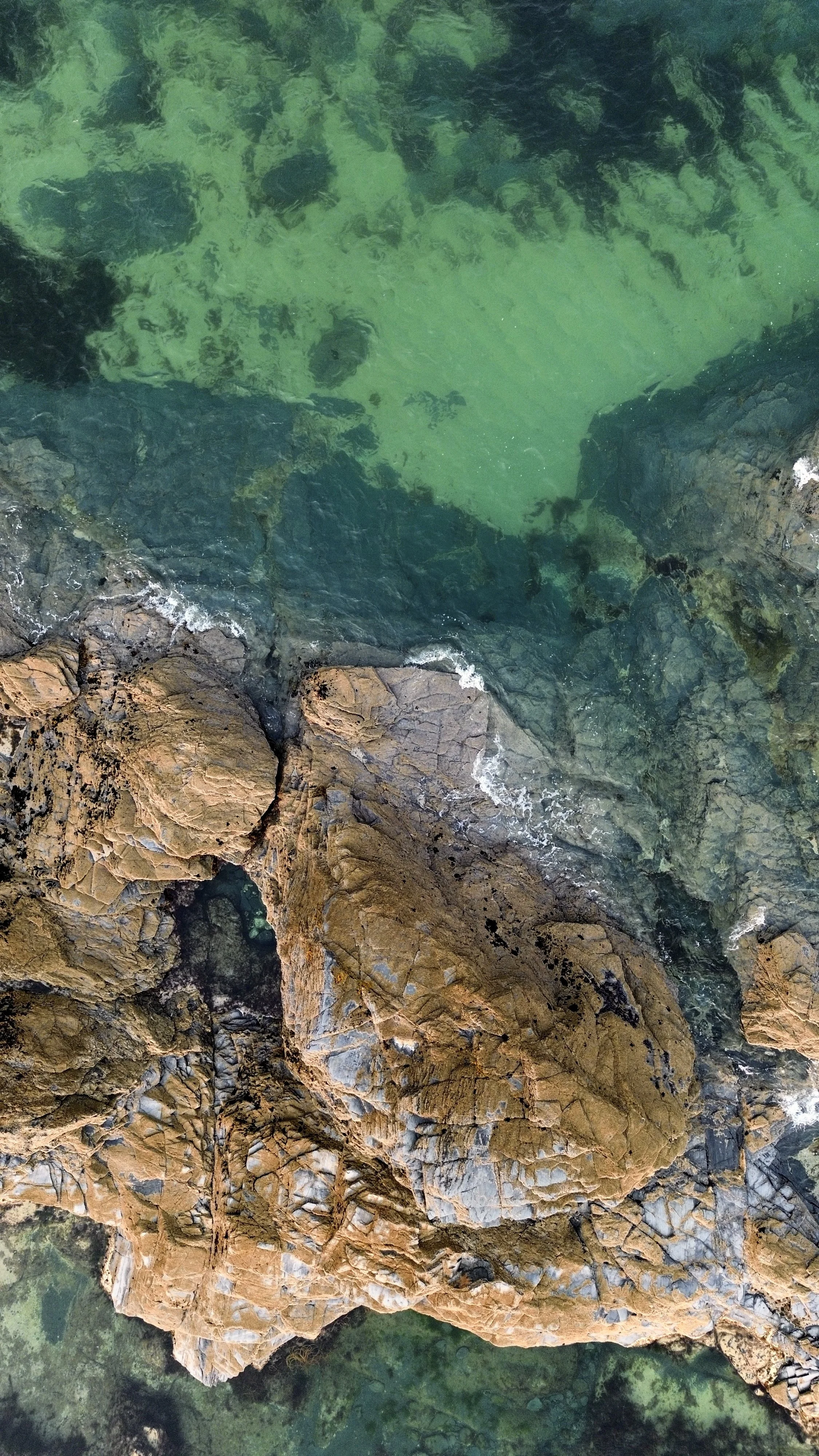A view of sandy beach with large rocks and clear blue-green ocean water.