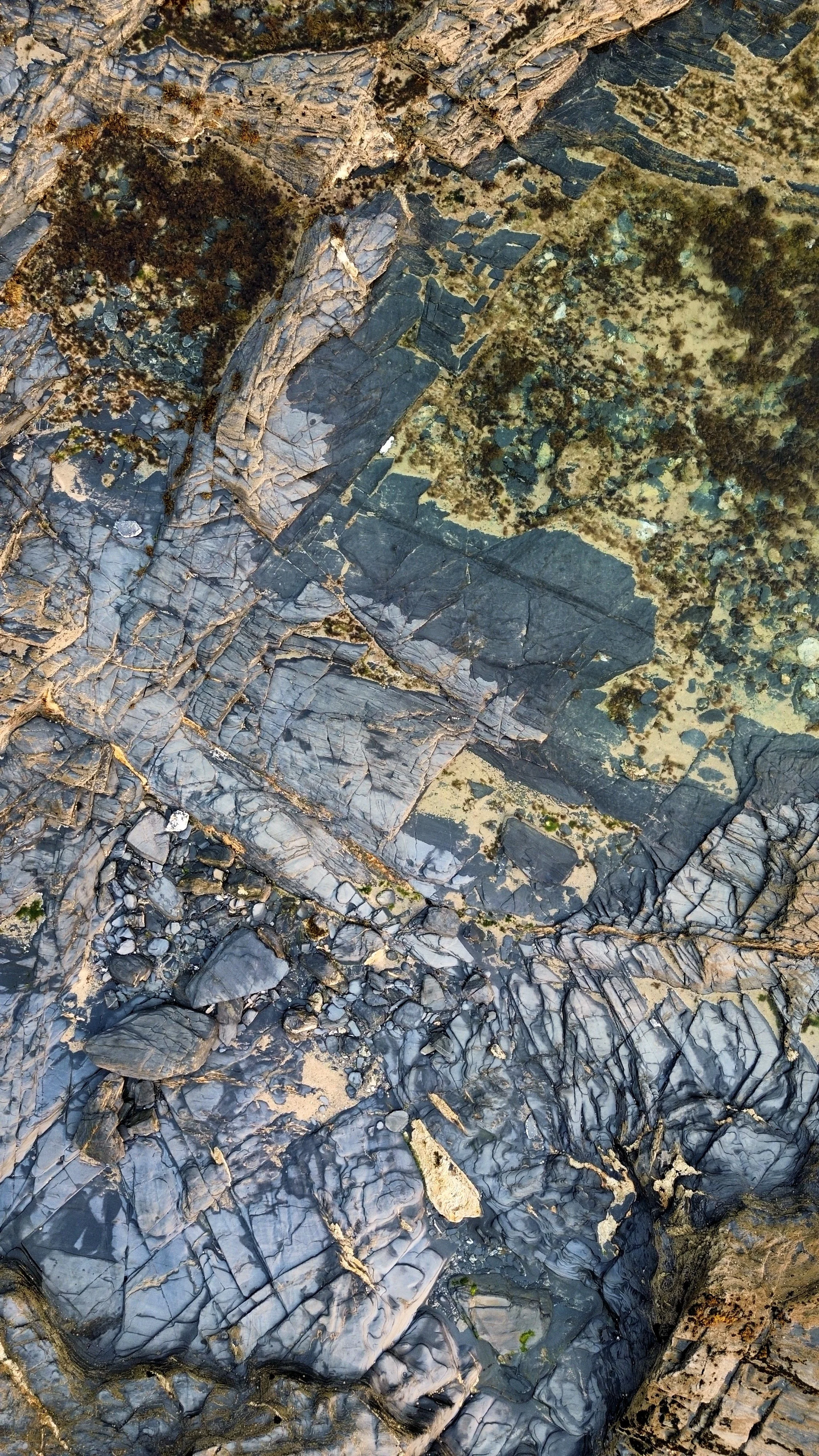 Aerial view of rocky terrain with layered stone formations, patches of moss, and sparse vegetation.
