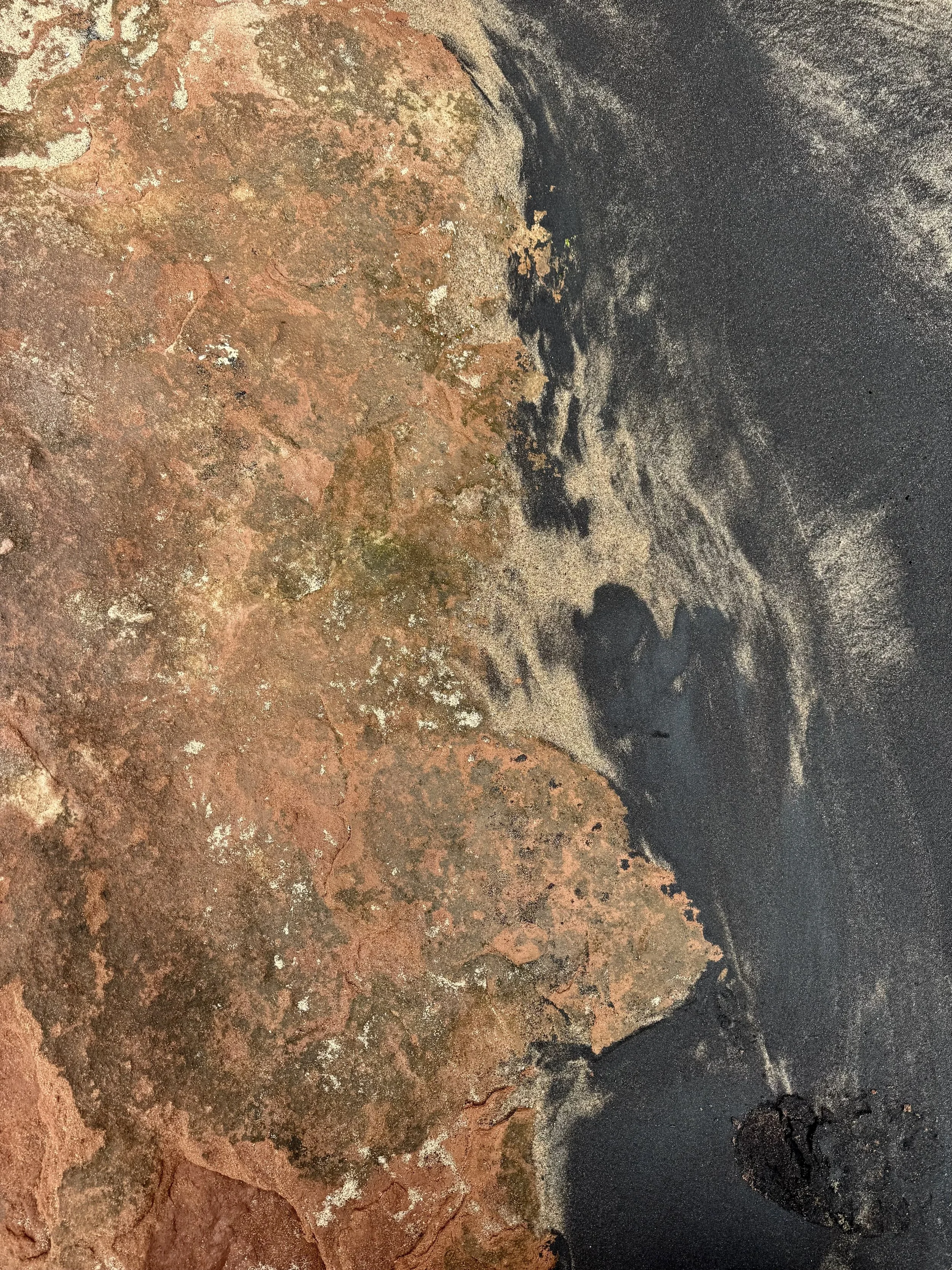 Close-up of a weathered, rocky surface with reddish-brown and blackish dark patches.