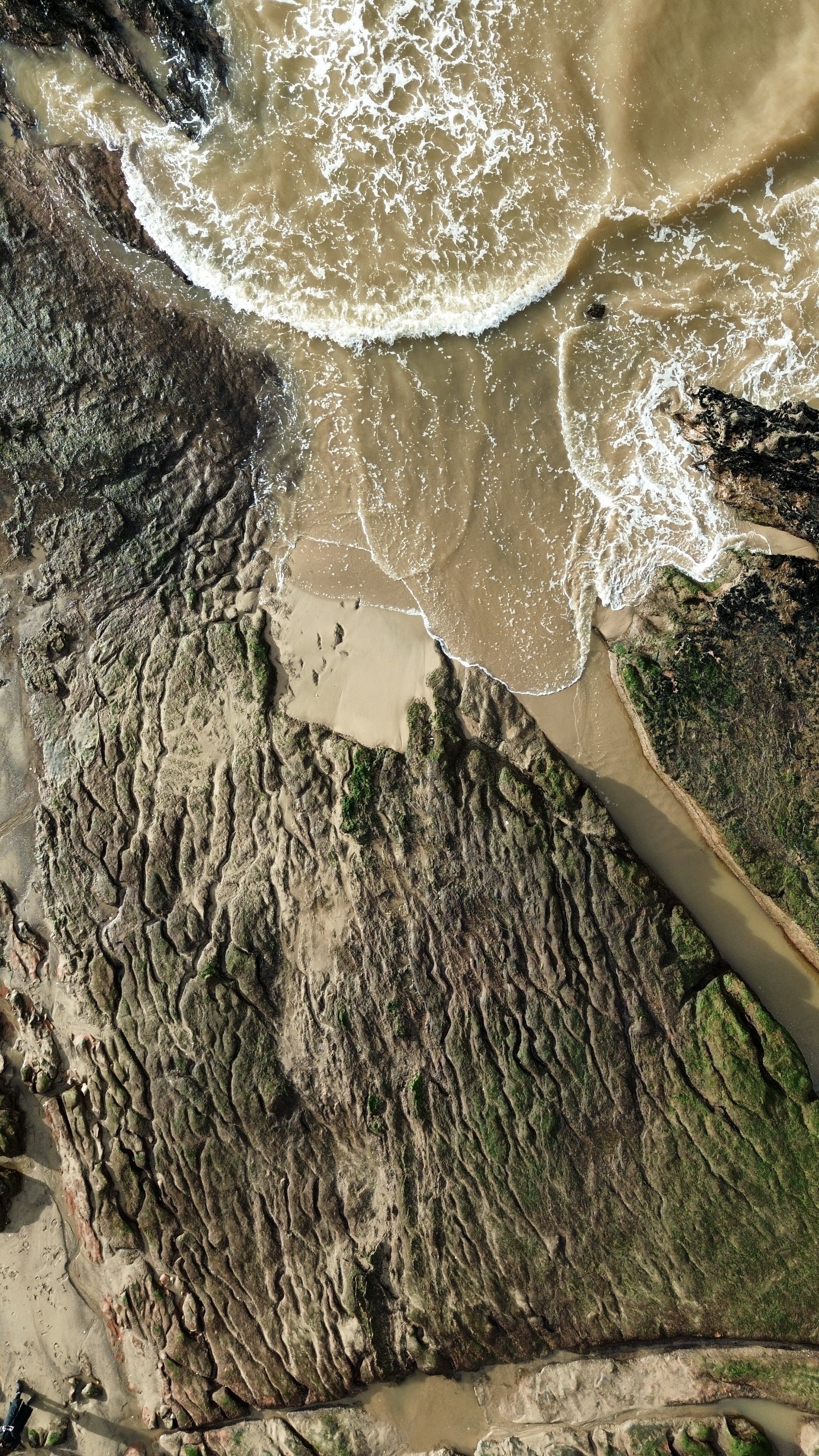 Aerial view of a rocky coastline with waves crashing against the rocks and sandy beach.