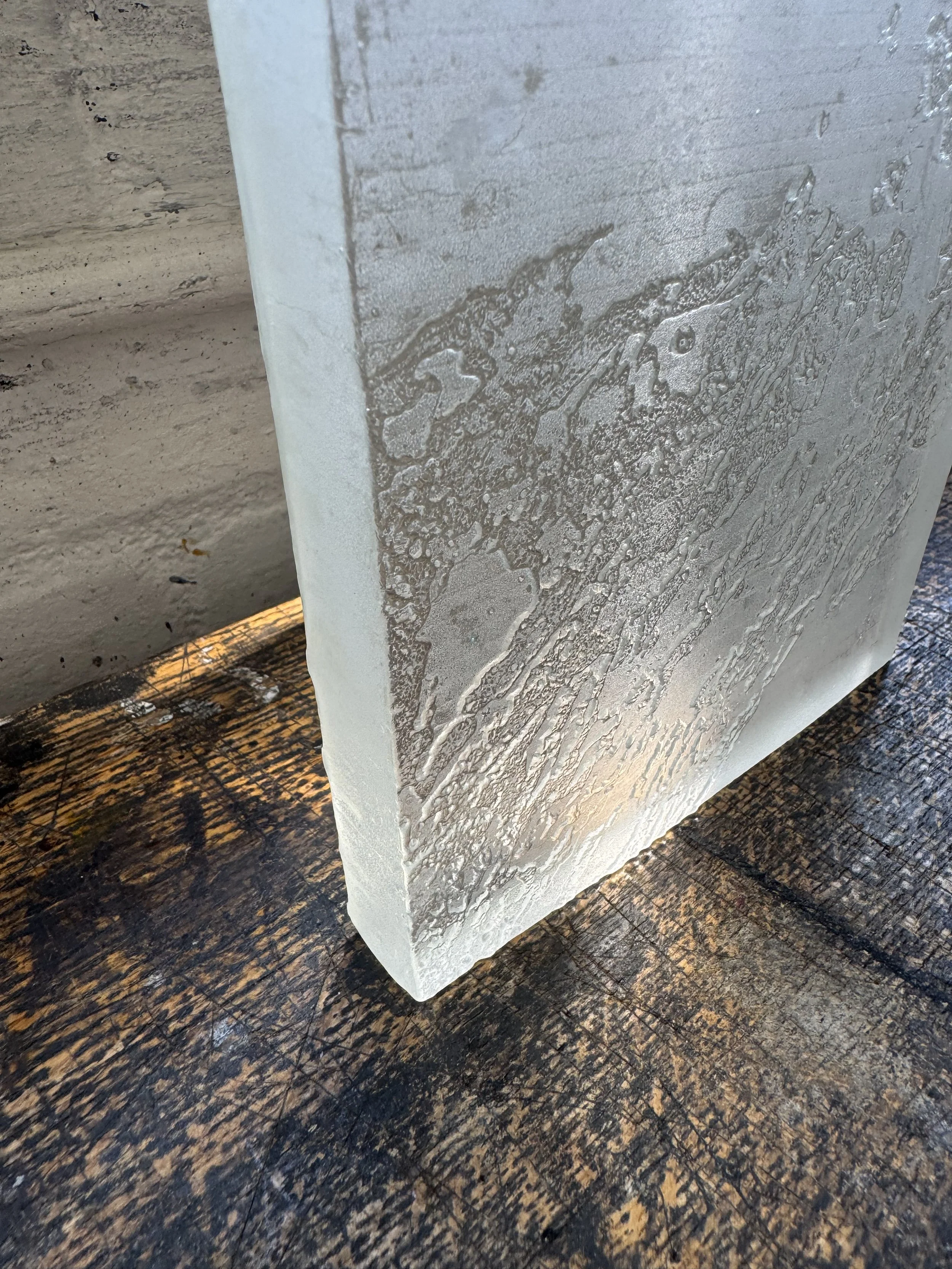 Close-up of a textured, grayish, rectangular stone or concrete block with water stains, sitting on a dark, weathered wooden surface.