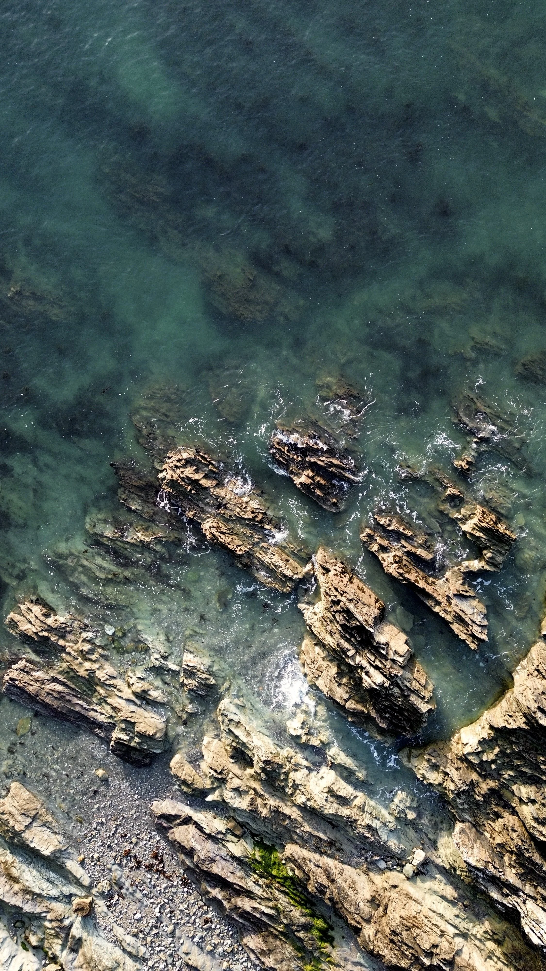 Aerial view of rocky shoreline with waves crashing against rugged rocks in the ocean.