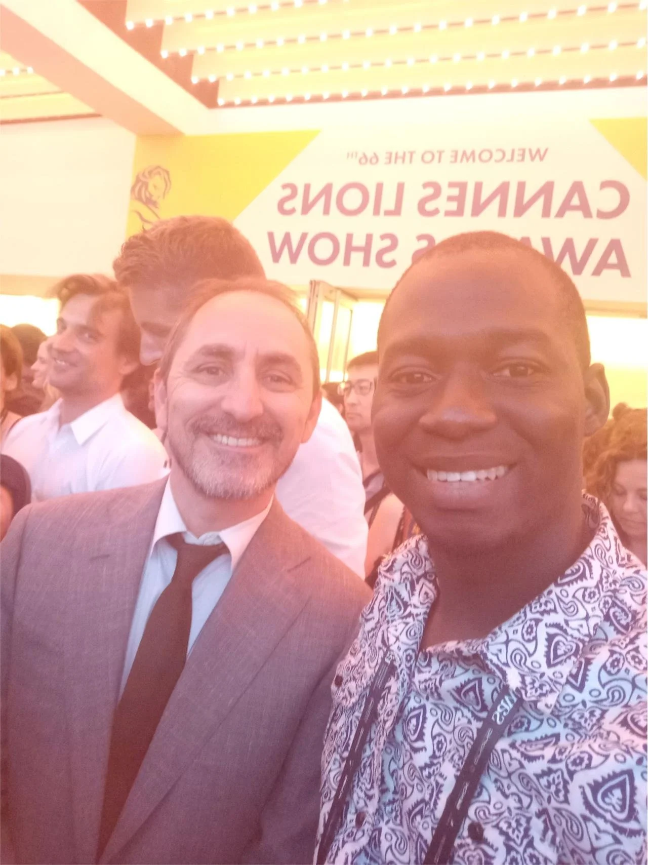 Sodiq Sheu and David Droga, two men smiling at a lively event, with a crowd behind them and a partially visible sign with the words "CANNES LIONS AWARDS SHOW" in the background.