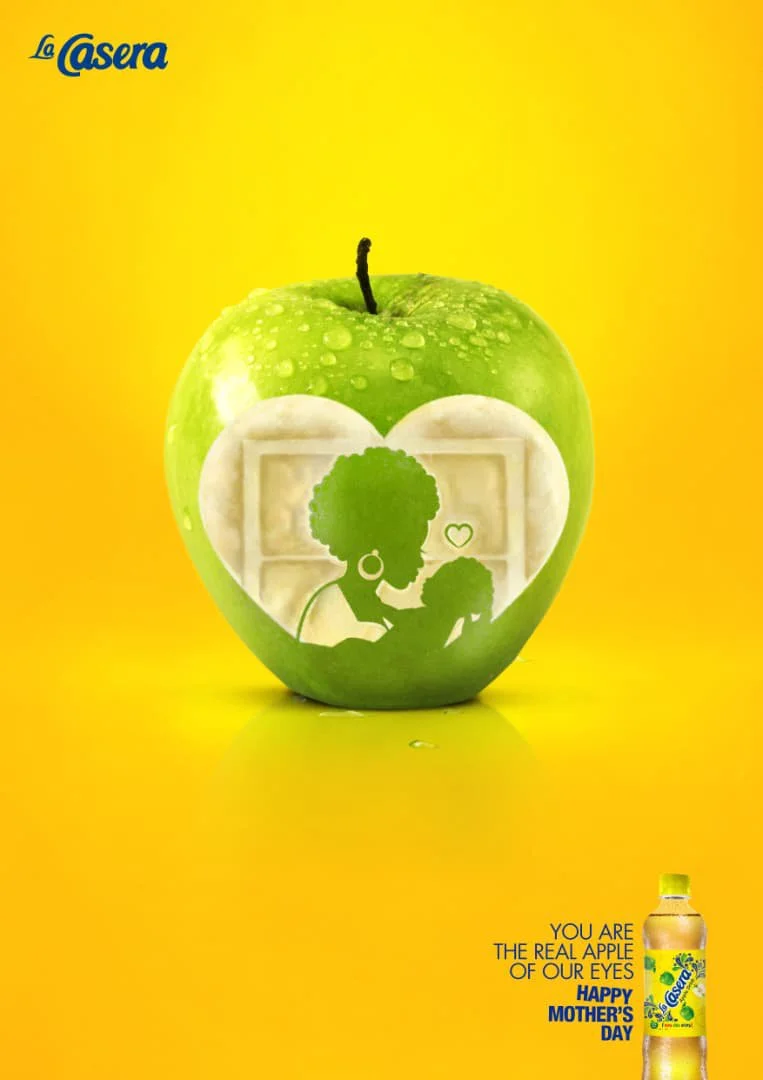An advertisement featuring a green apple with a silhouette of a woman and child carved into the apple, with the woman holding the child's hand. The background is yellow, and there's a bottle of La Casera drink in the bottom right corner with text cel
