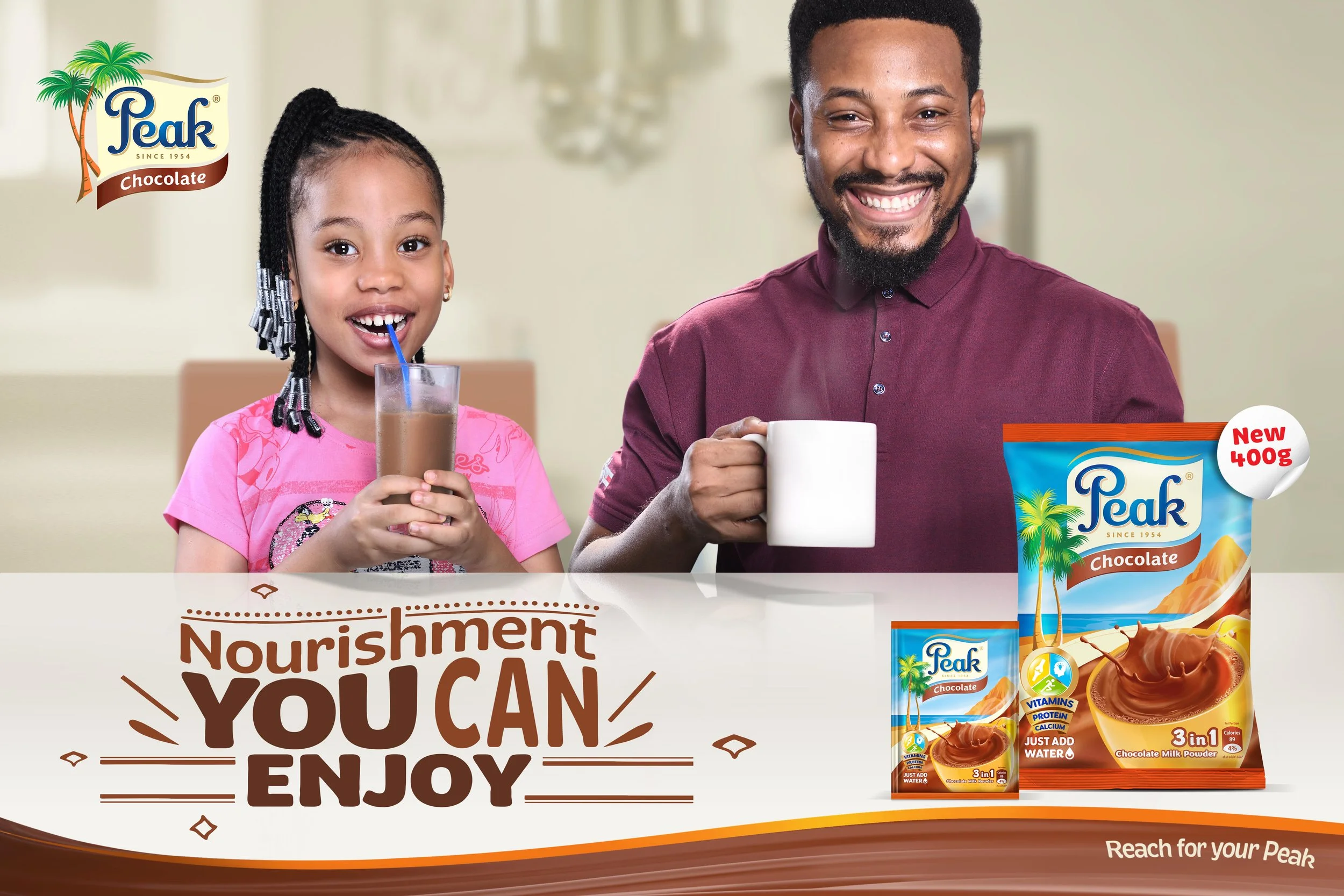 A man and young girl smiling while drinking chocolate flavored beverage in a bright home. The girl has braided hair and wears a pink shirt, the man has a beard and wears a maroon shirt. The image advertises Peak chocolate milk powder.