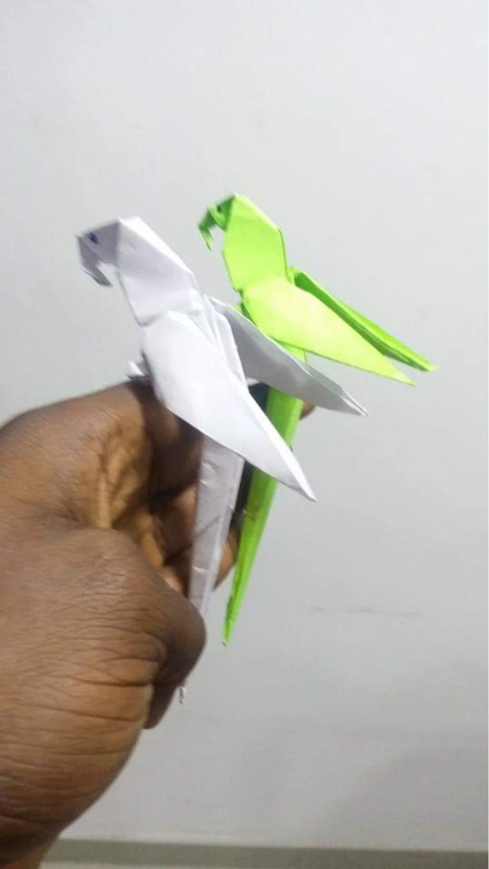 Hand holding two paper origami birds, one white and one neon green, against a plain white background.