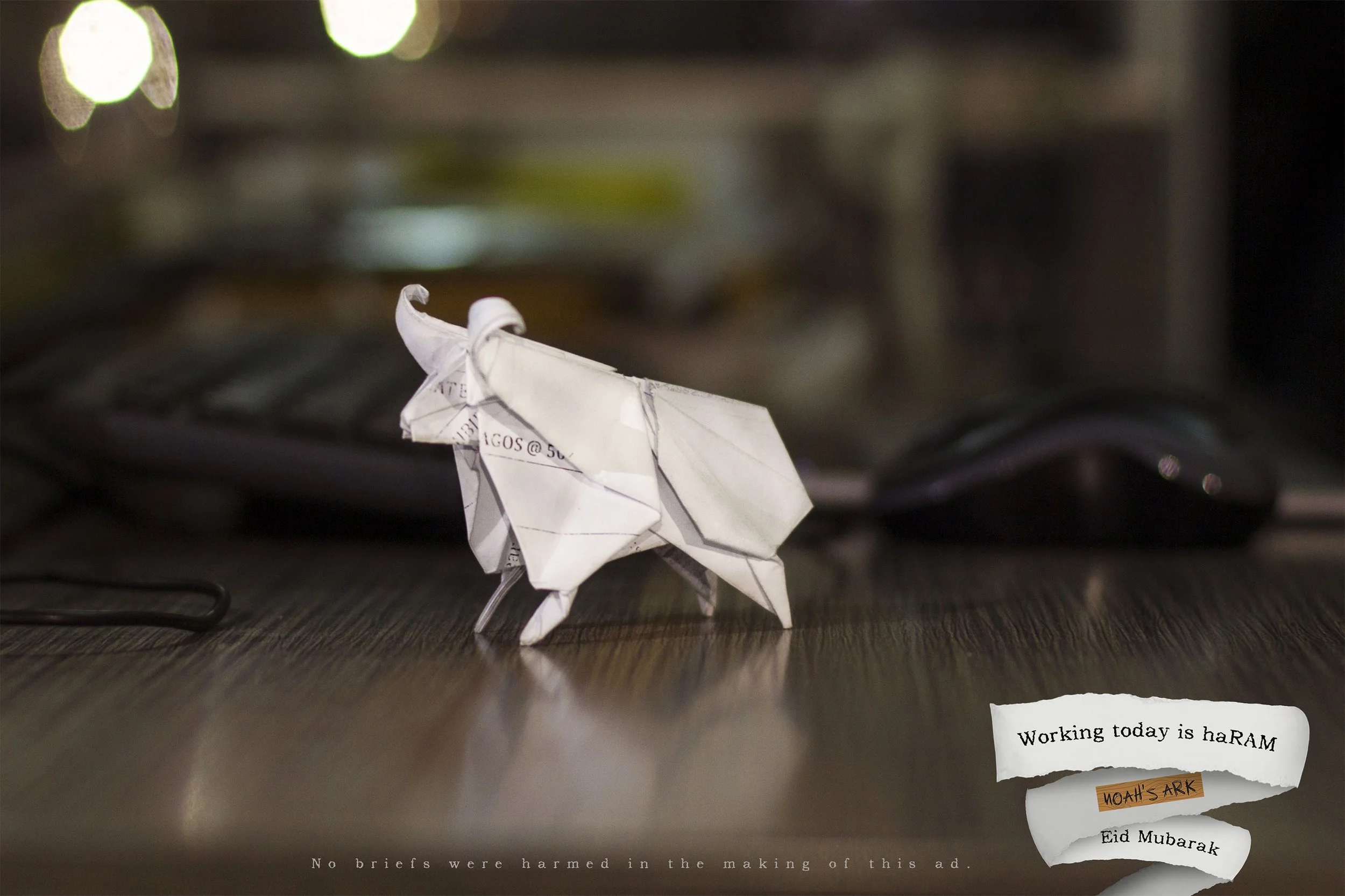 A crumpled paper origami butterfly on a wooden surface with a blurred background and torn paper notes attached. One note says, "working today is haRAM" and another says, "NOAH'S ARK."