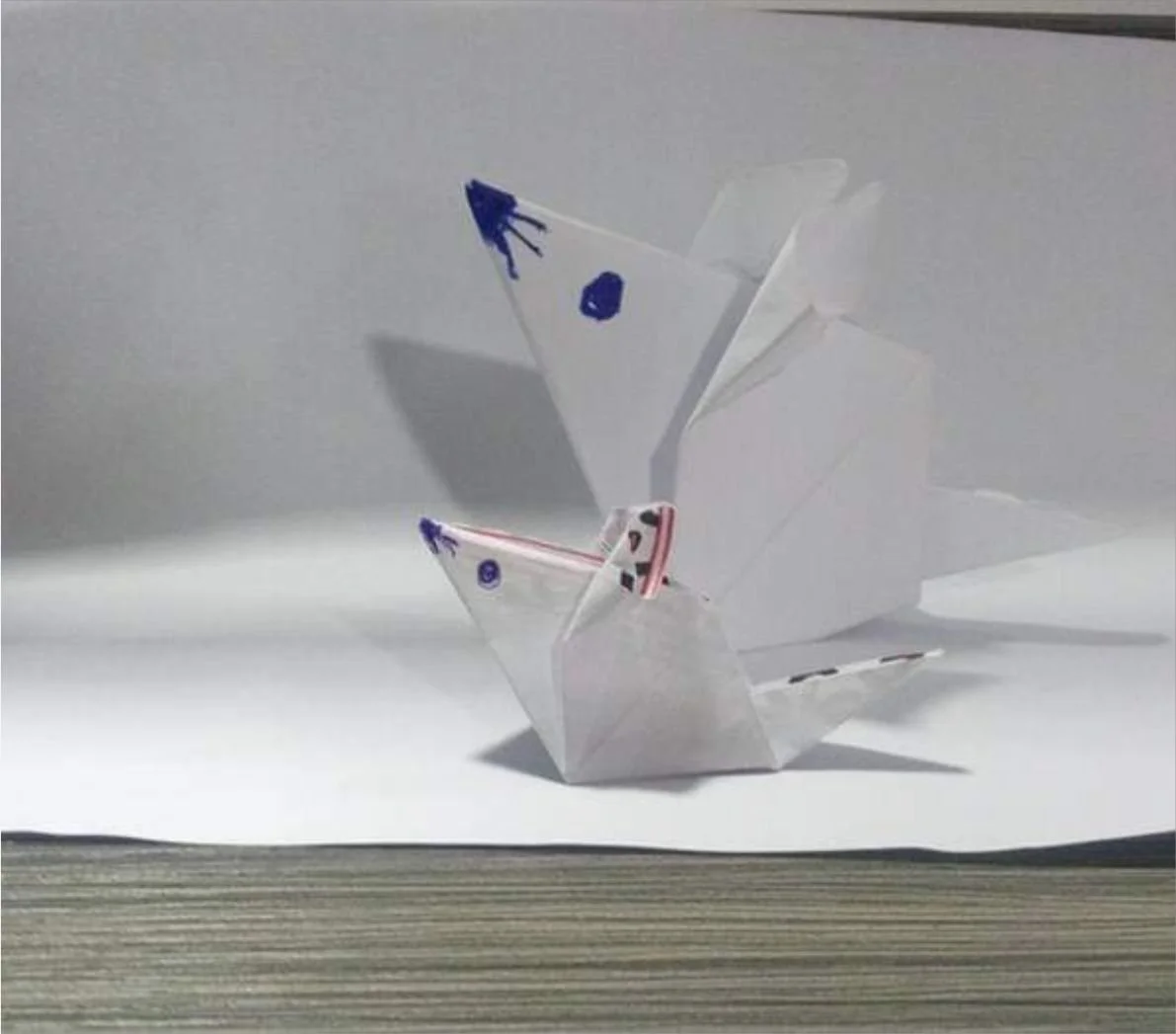 Origami paper swan made from white paper with blue and purple markings, placed on a white surface with a plain white background.