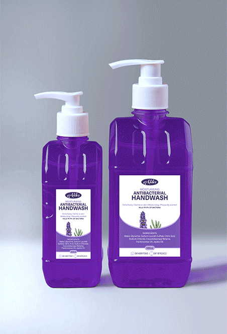 Two purple bottles of antibacterial handwash with white pump dispensers, one larger and one smaller, placed on a gray surface against a light-colored background.