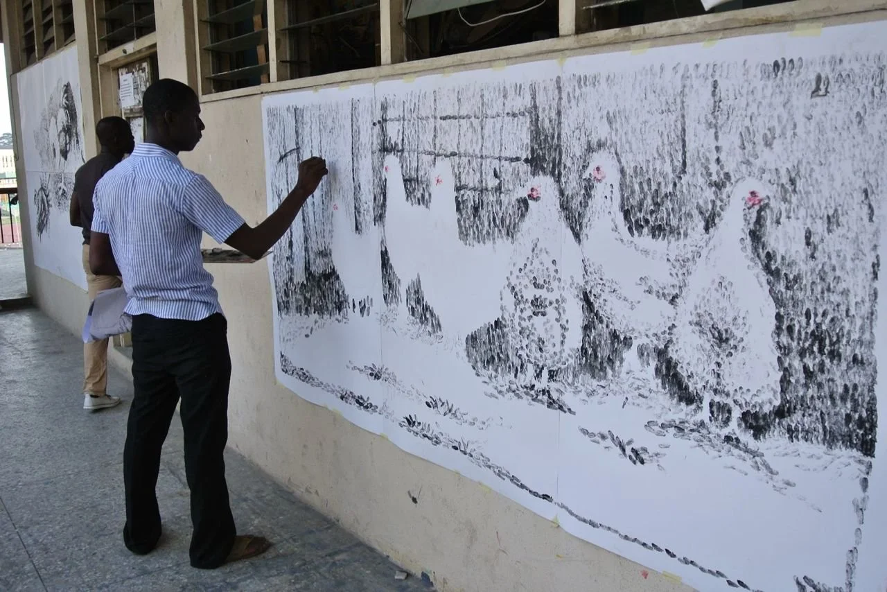 A person painting an image of four chickens on a large outdoor wall, next to a window with bars, with another person observing in the background. Ayinde Okin. Nigeria Artist.