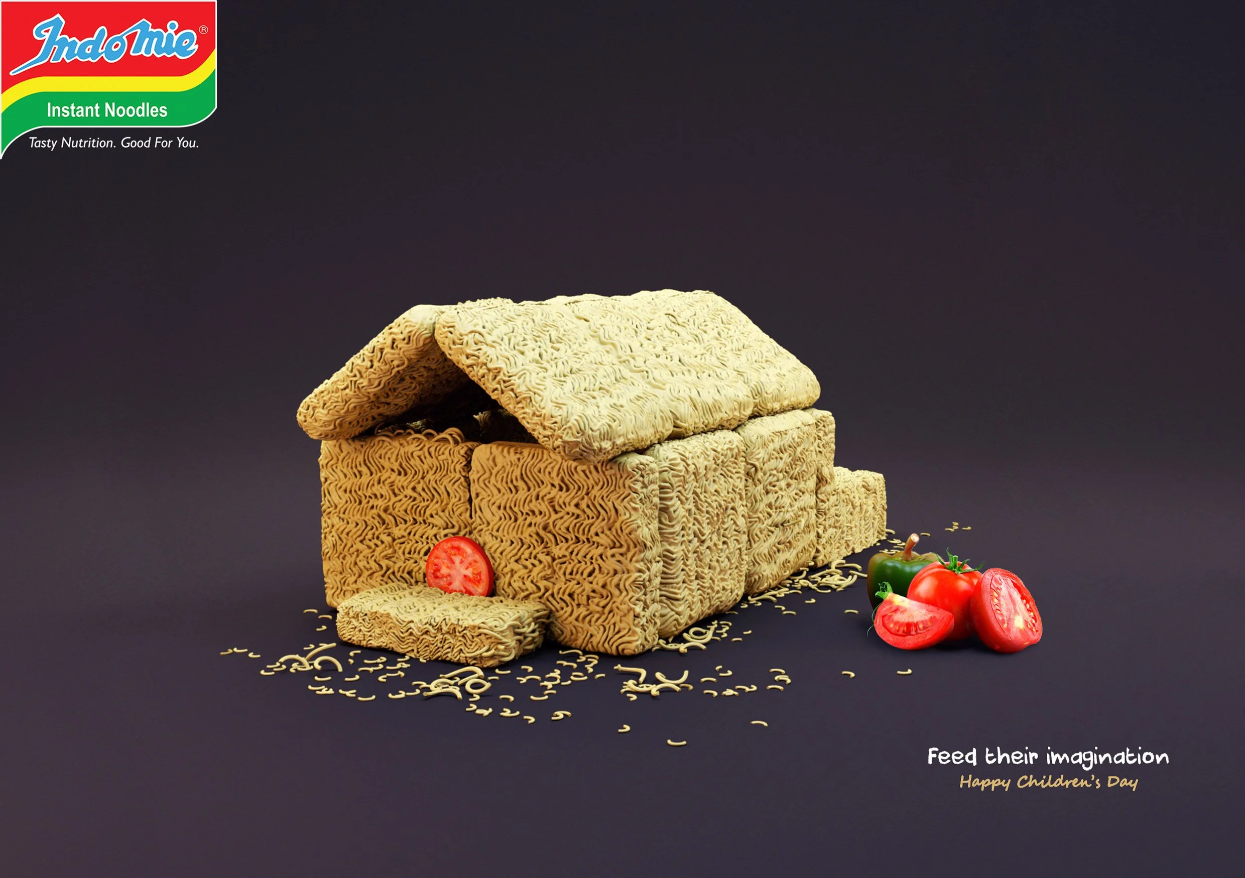 A box of uncooked instant noodles with some sliced tomatoes and a green chili on the side, set against a black background. The box has a red, yellow, green, and blue logo in the upper left corner. There is a message in the lower right corner that says, "Feed their imagination" and "Happy Children's Day."