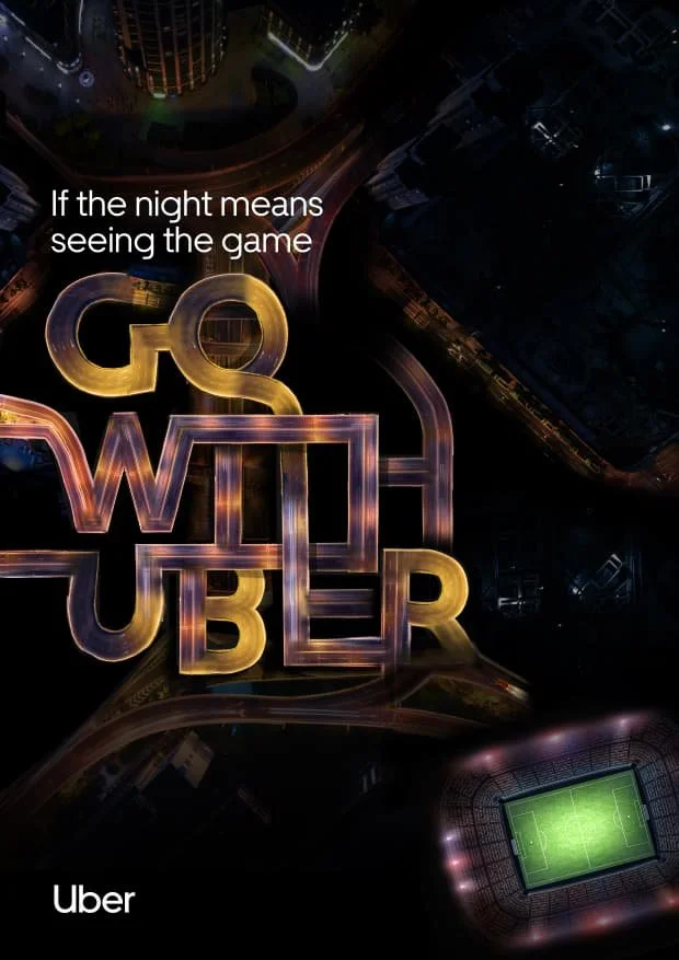 Night aerial view of a city with illuminated signs reading "GO WILD Uber" and a lit soccer stadium.