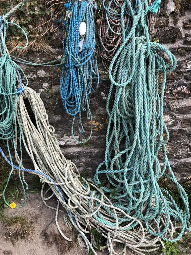 Multiple colorful ropes hanging and tangled on a stone wall with some grass and a small yellow flower at the bottom left.