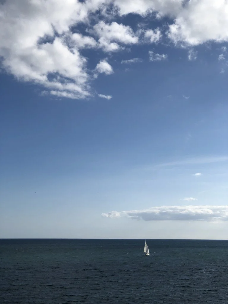 A sailboat sailing on the ocean under a partly cloudy sky in daytime.