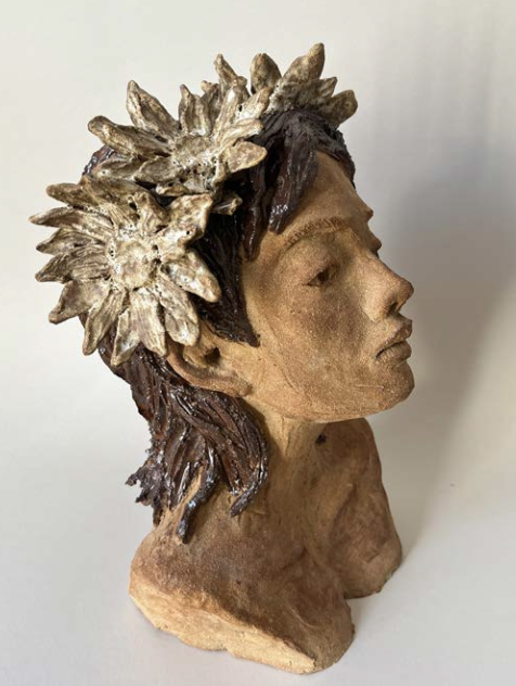 Sculpture en terre cuite représentant une tête humaine de profil avec une couronne de fleurs ou de feuilles sur la tête.