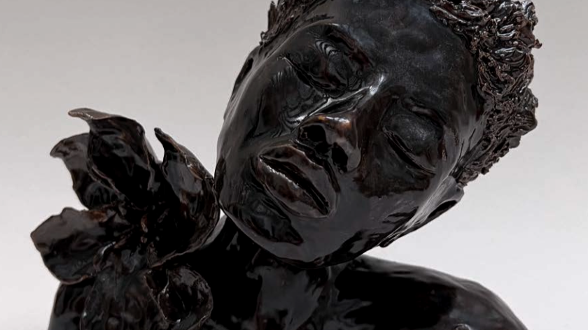 Sculpture en bronze représentant un visage féminin avec des yeux fermés et un détail floral ou végétal près du visage.