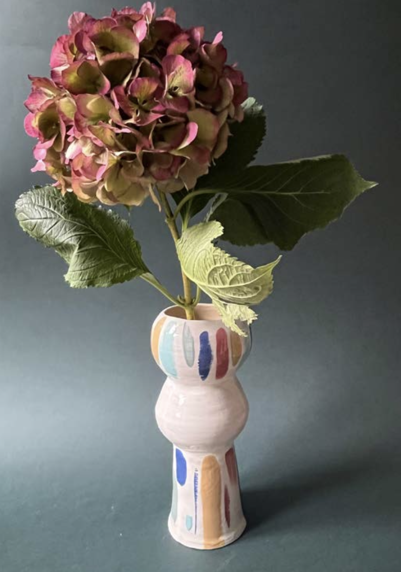 Hortensia colorée dans un vase en céramique avec des motifs colorés, posé sur un fond vert foncé.
