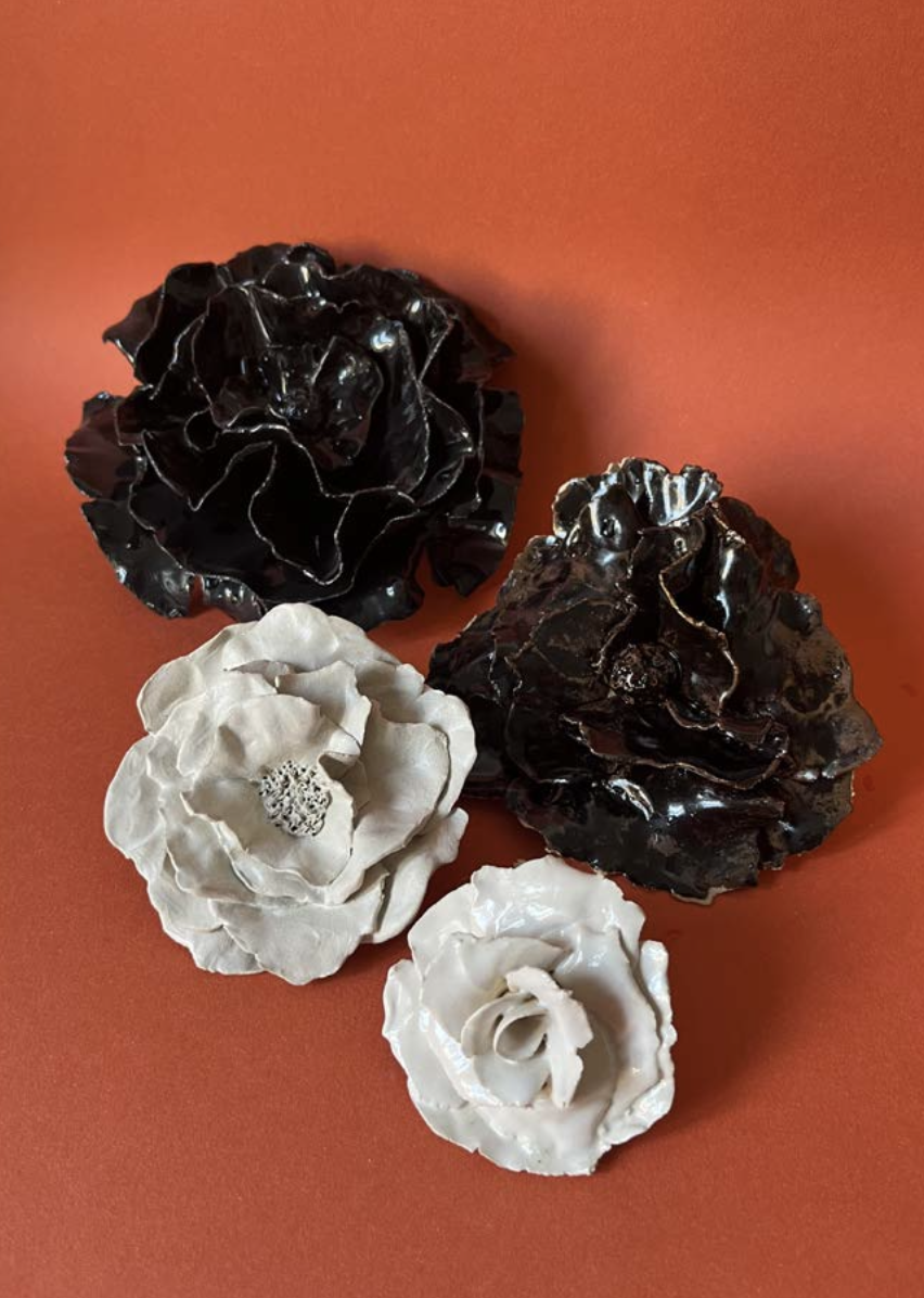 Cinq fleurs décoratives en forme de roses, en couleurs noir et blanc, posées sur une surface orange.