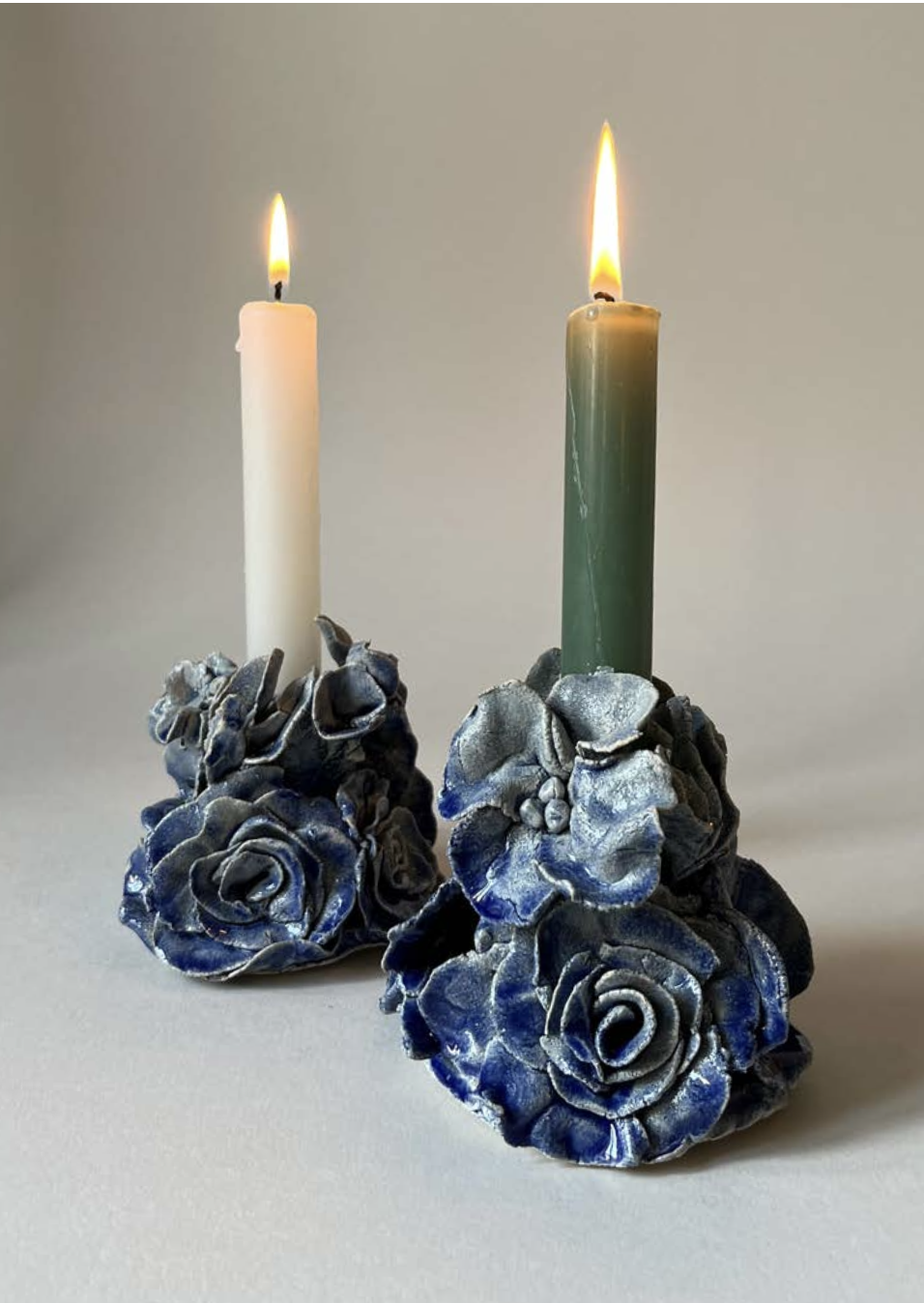 Deux chandelles allumées sur des porte-chandelles décorés de roses en céramique bleue.