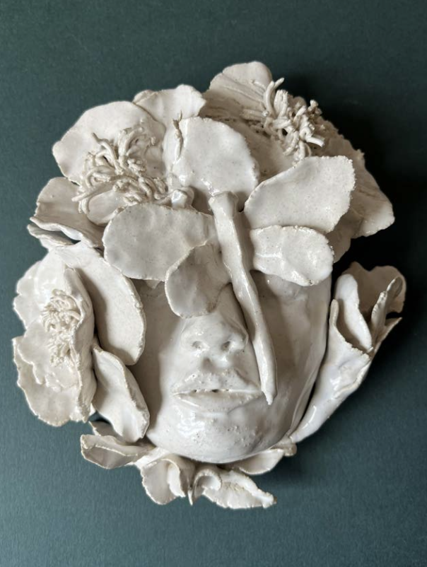 Sculpture en céramique représentant un visage humain avec des éléments floraux ou végétaux intégrés.